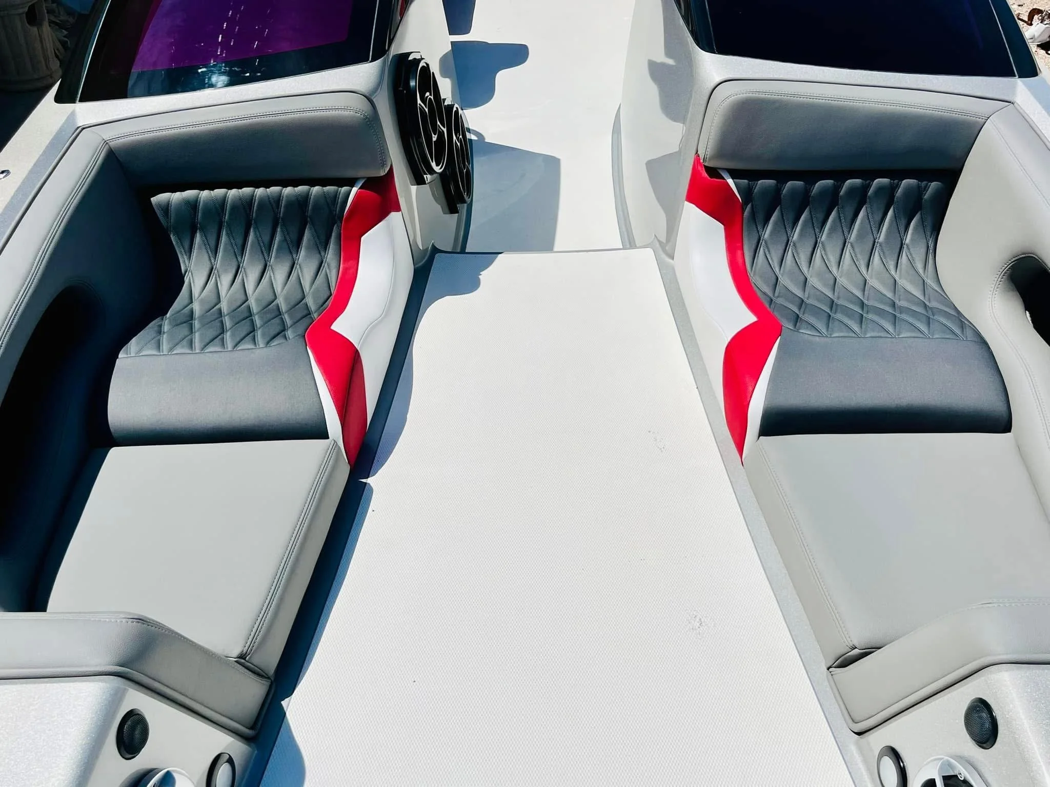 Two boat seats with grey, black, and red upholstery on a white boat deck, with two black speakers and a black vent visible.