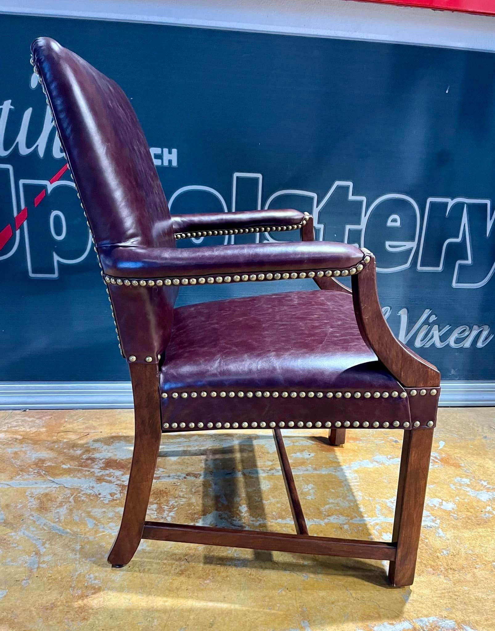 A vintage-style armchair with wooden frame and burgundy leather upholstery, accented with brass nailhead trim.