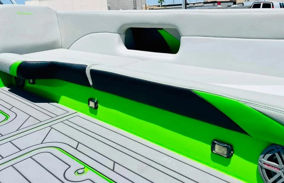 Close-up of a boat's interior with white, green, and black cushioned seating and a textured deck featuring green accents.