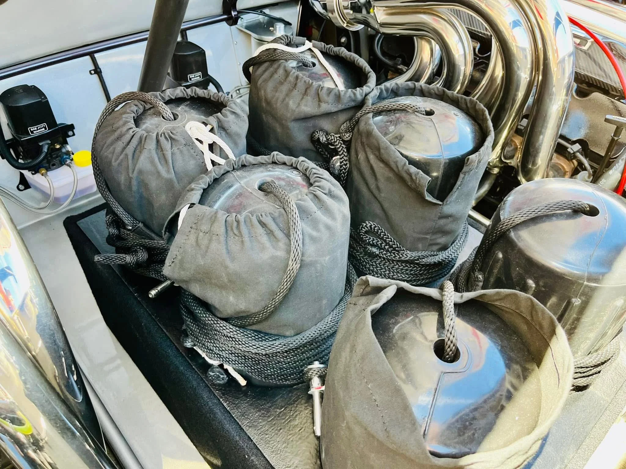 Multiple black fuel cell bladders with braided hoses and metal fittings inside a race car's engine bay.