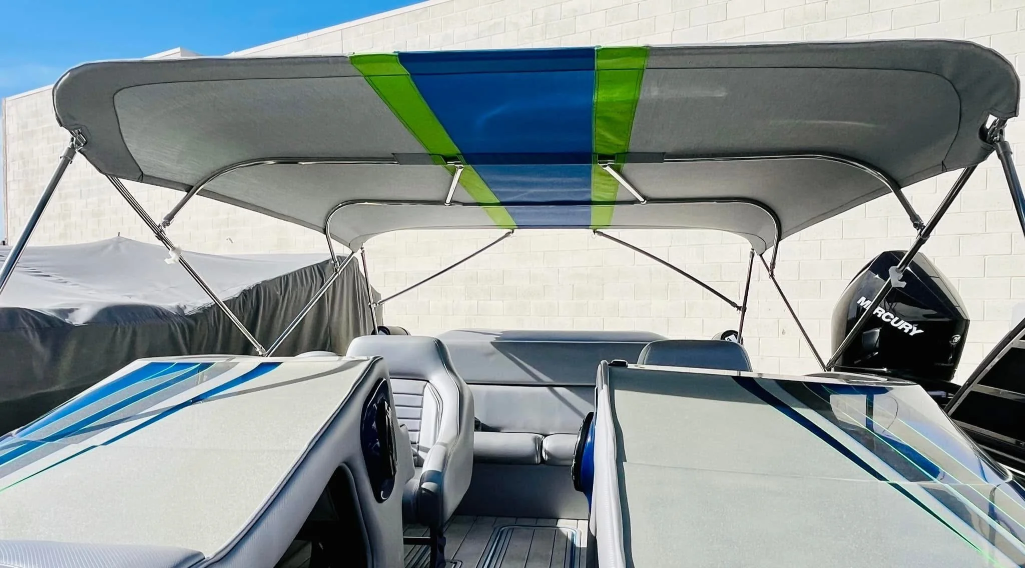 A boat with a canopy and a Mercury outboard motor parked near a white wall.
