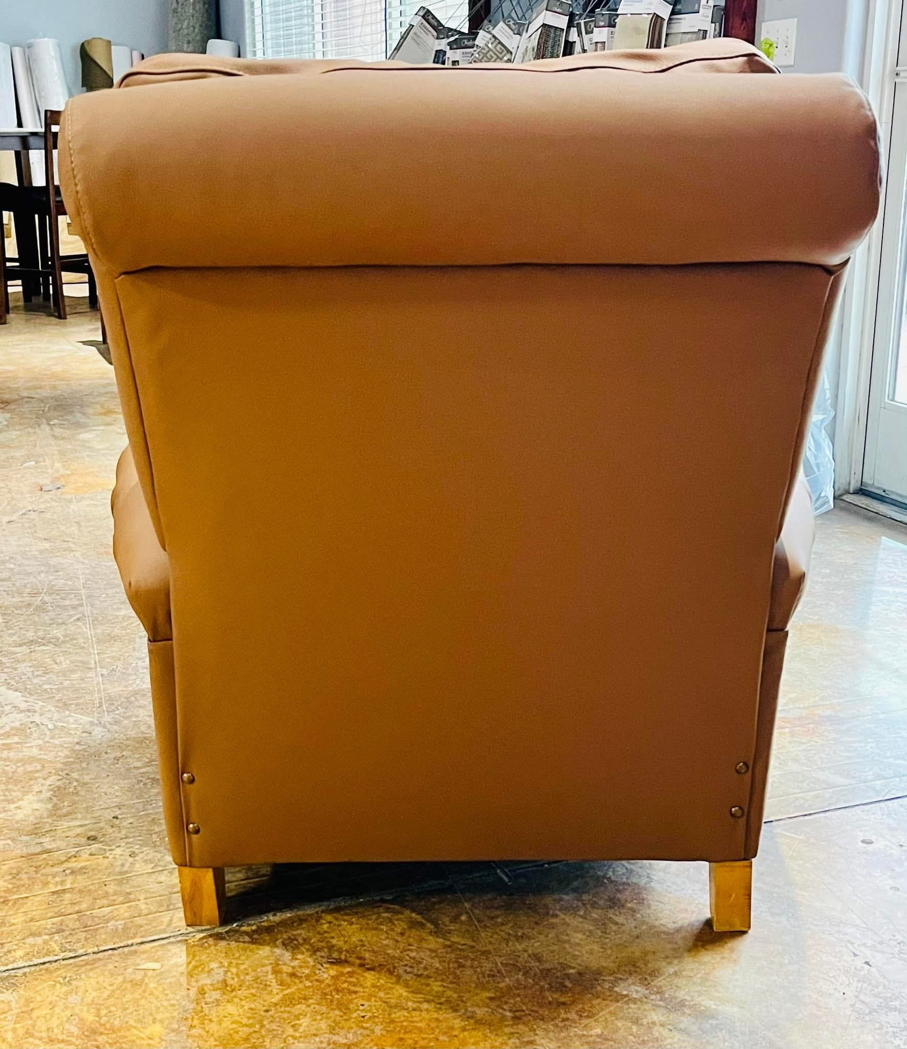 Back view of a brown leather armchair on a wood floor in a room with bookshelves and a window.
