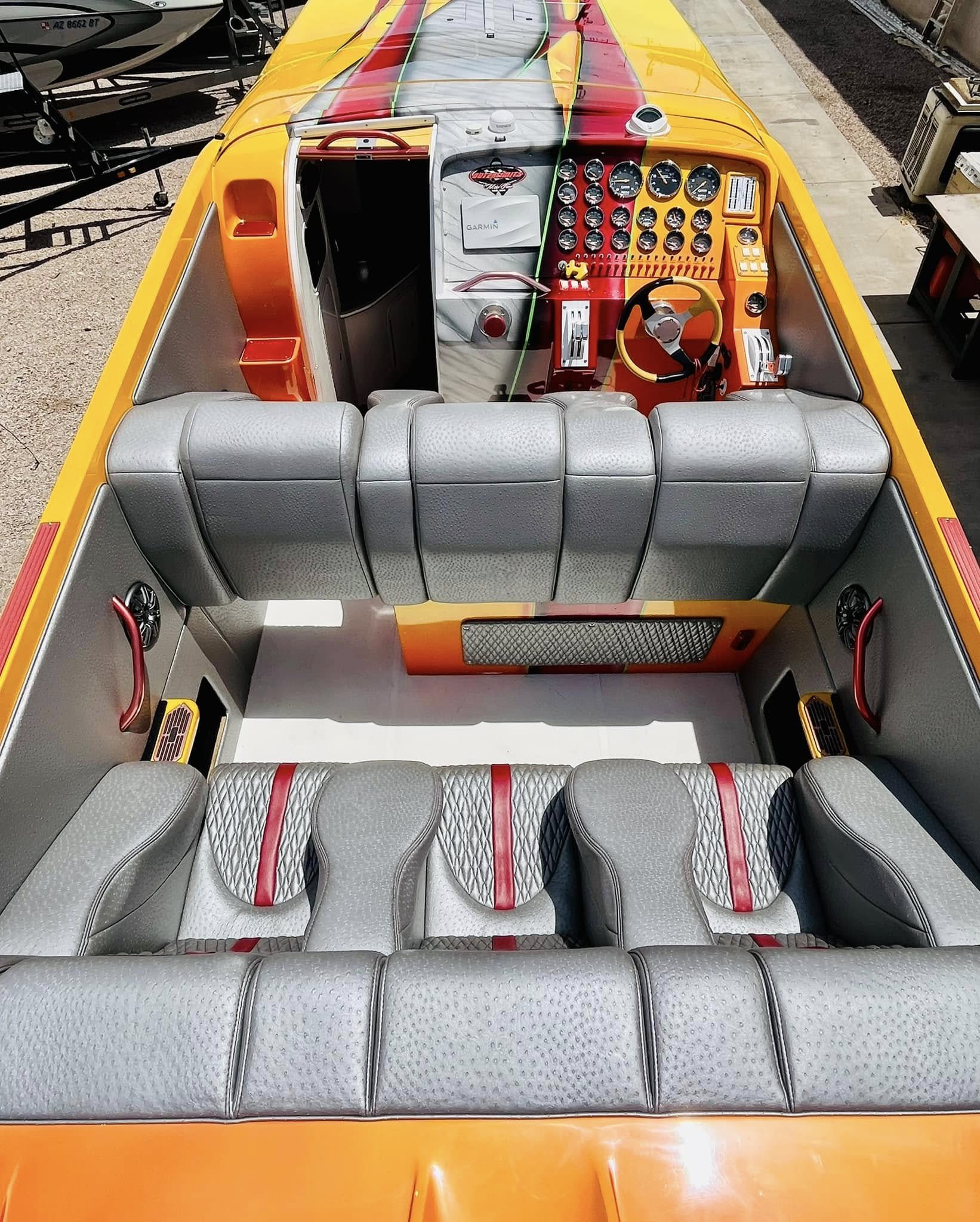 Interior of a colorful speedboat with gray seats, dashboard with various gauges, steering wheel, and electronics.
