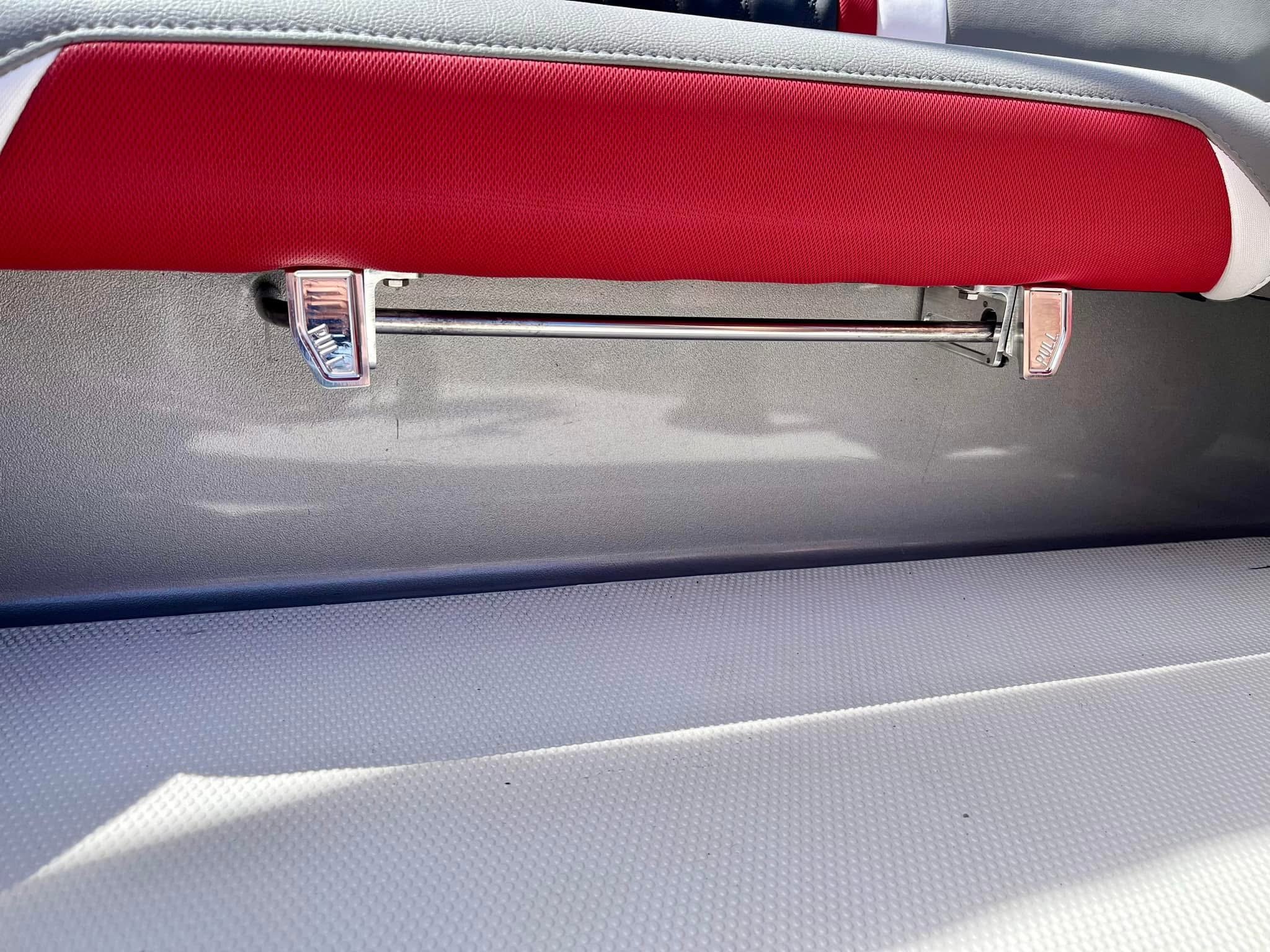 Back of a gray bus seat with a red leather headrest and a metal grab bar.