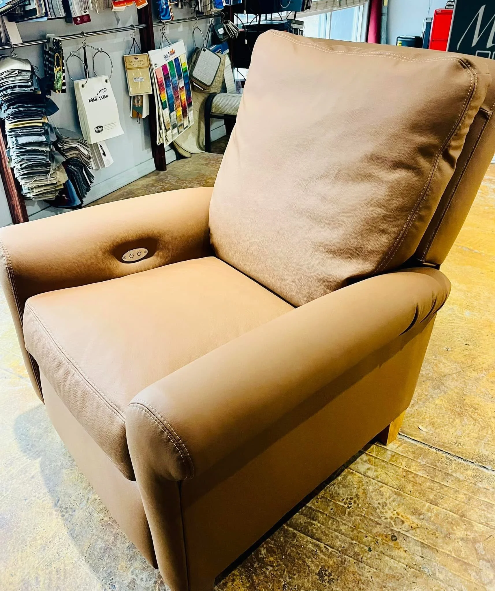 A beige recliner chair with a remote control attached to the right armrest, situated in a furniture or home goods store.