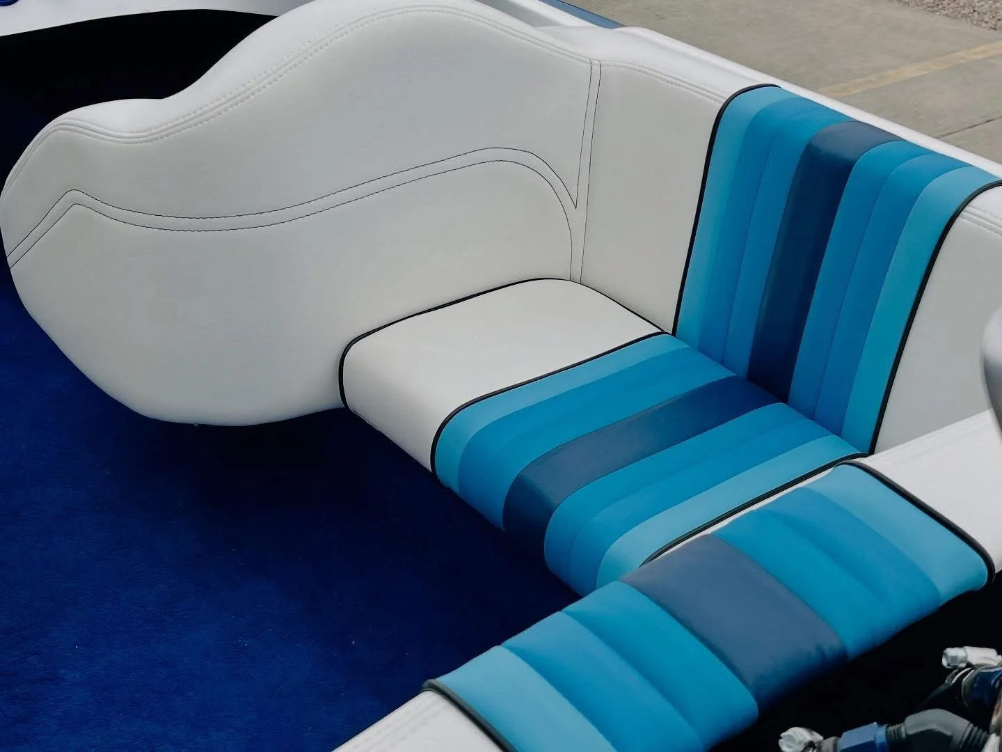 Close-up of a boat seat with white leather cushioning and blue striped fabric in varying shades, set against a dark blue carpeted floor.