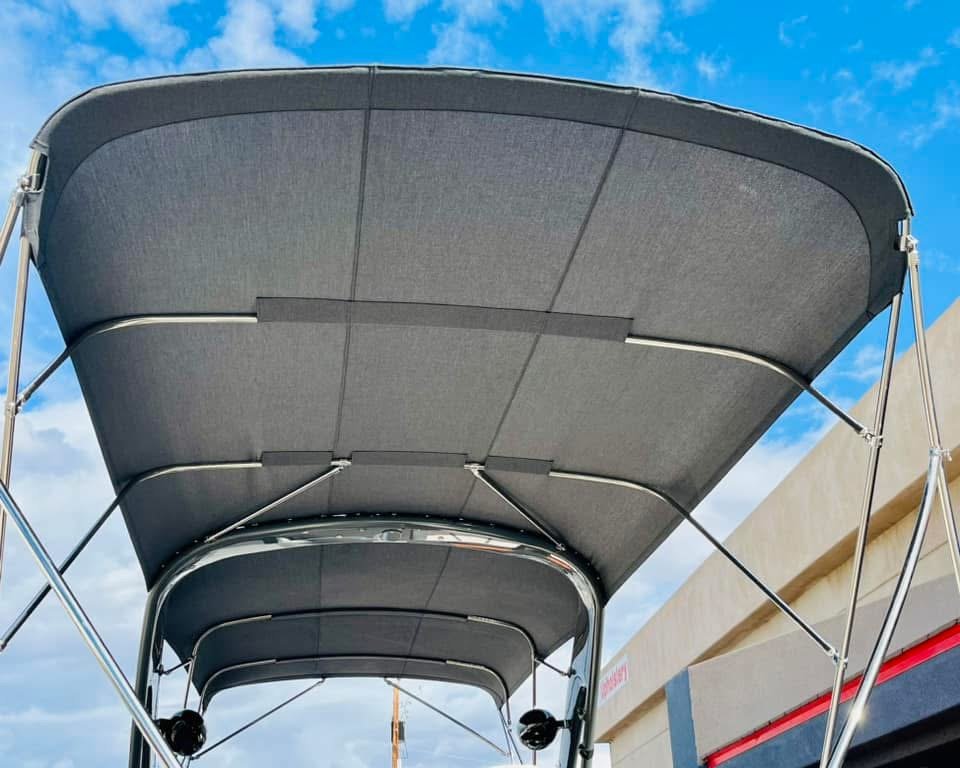 A boat with a gray canopy, viewed from below, during daytime. The boat is outdoors with a blue sky and some clouds in the background.