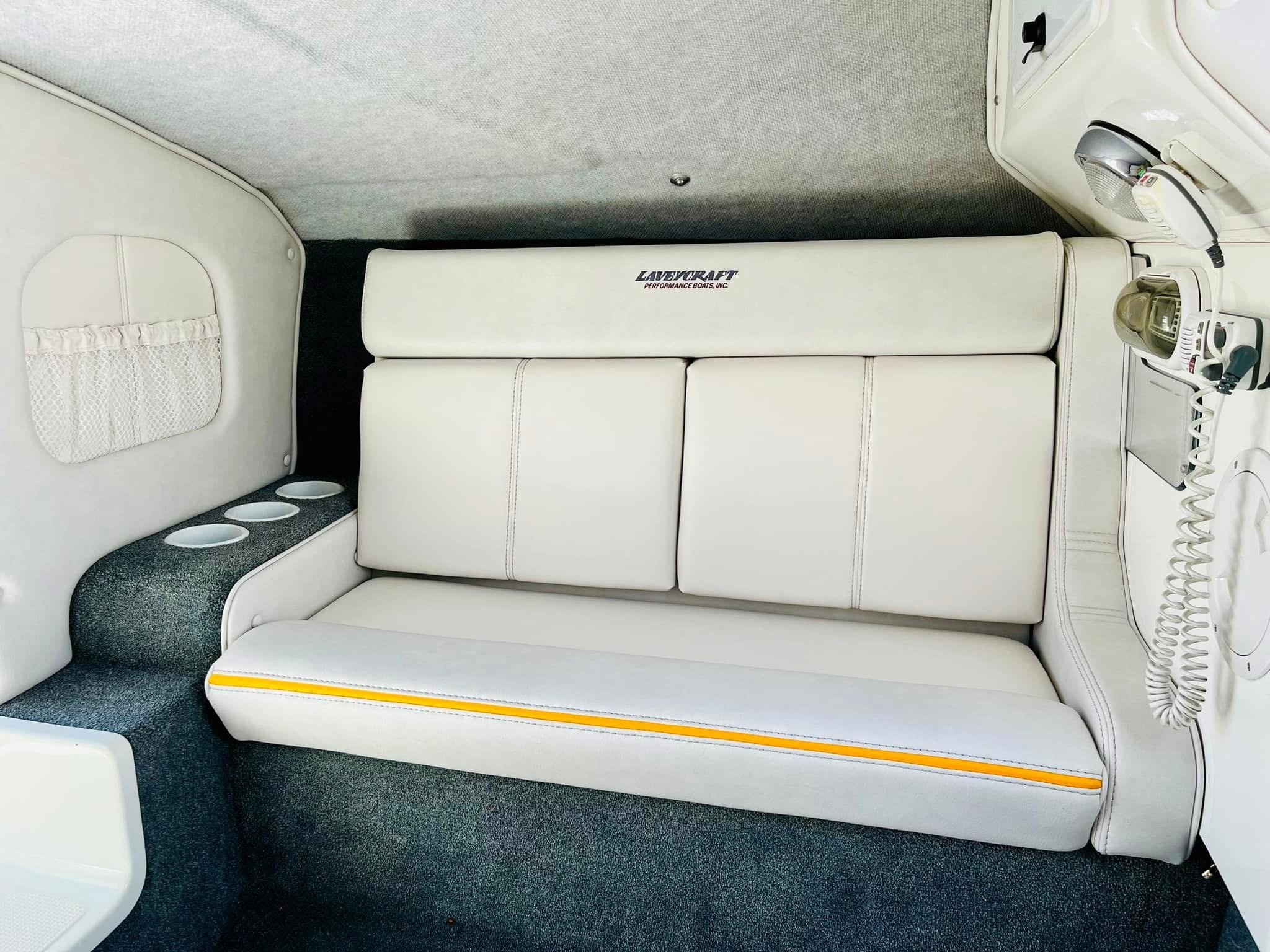 White leather seating area with built-in cup holders, a part of boat interior, with radio and electronic devices on the side.
