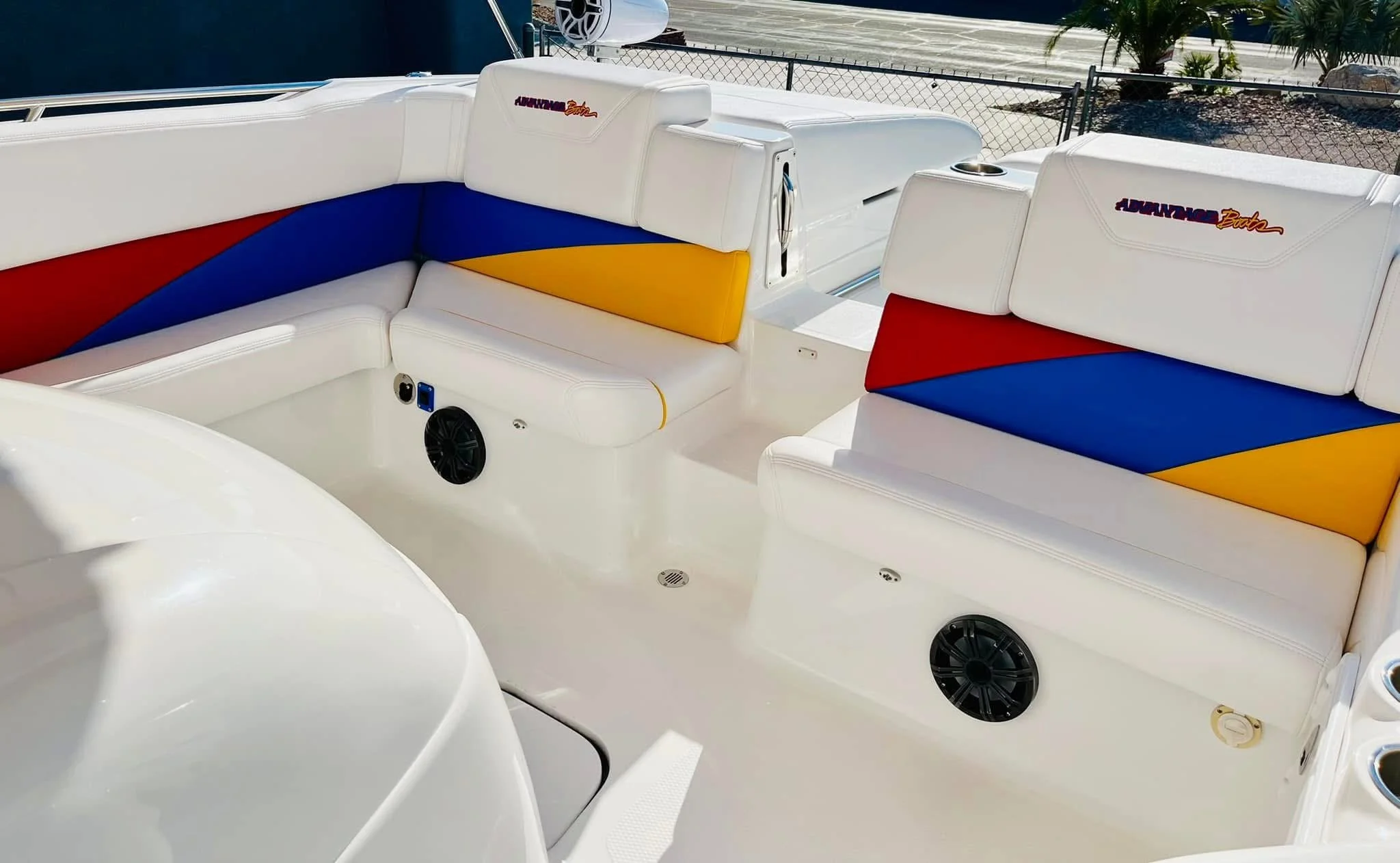 The interior of a boat featuring white seating with colorful geometric patterns in red, blue, and yellow, equipped with built-in speakers and a small storage compartment.