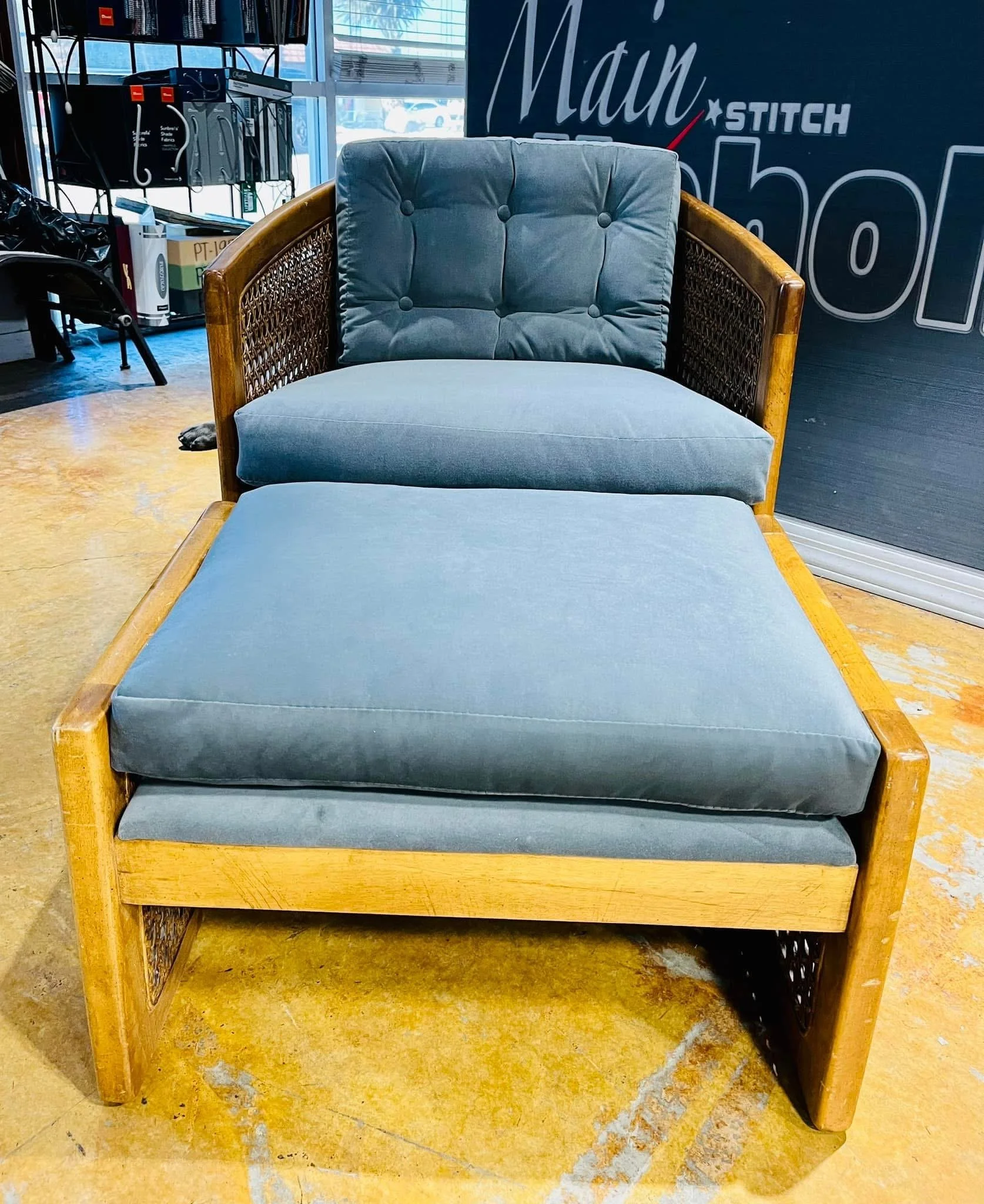 A blue and grey upholstered armchair with wooden frame and armrests, placed on a yellowish floor inside a store.