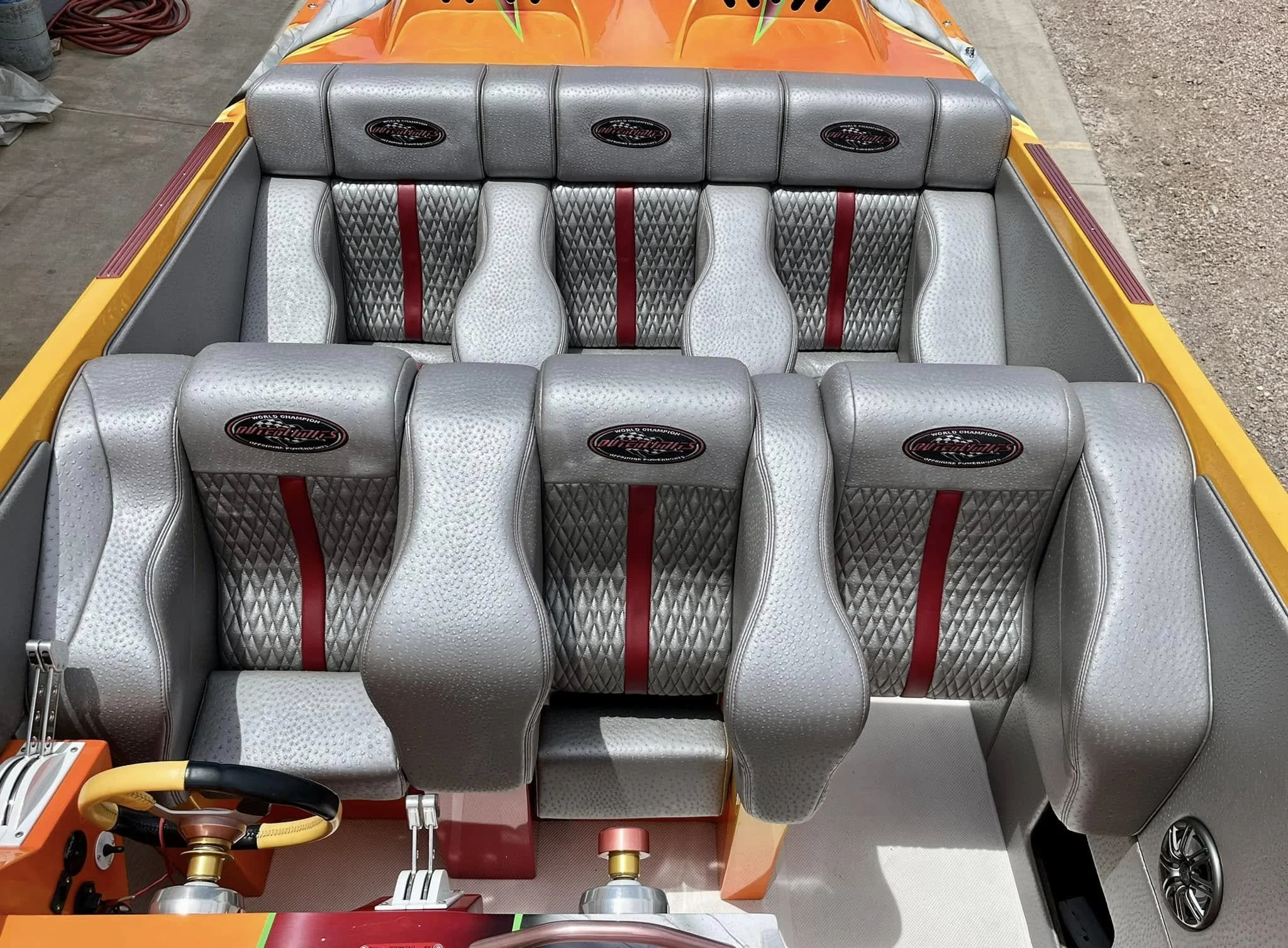 Interior of a colorful race car with several silver seats, each with a red stripe and diamond pattern, and a black and yellow steering wheel.