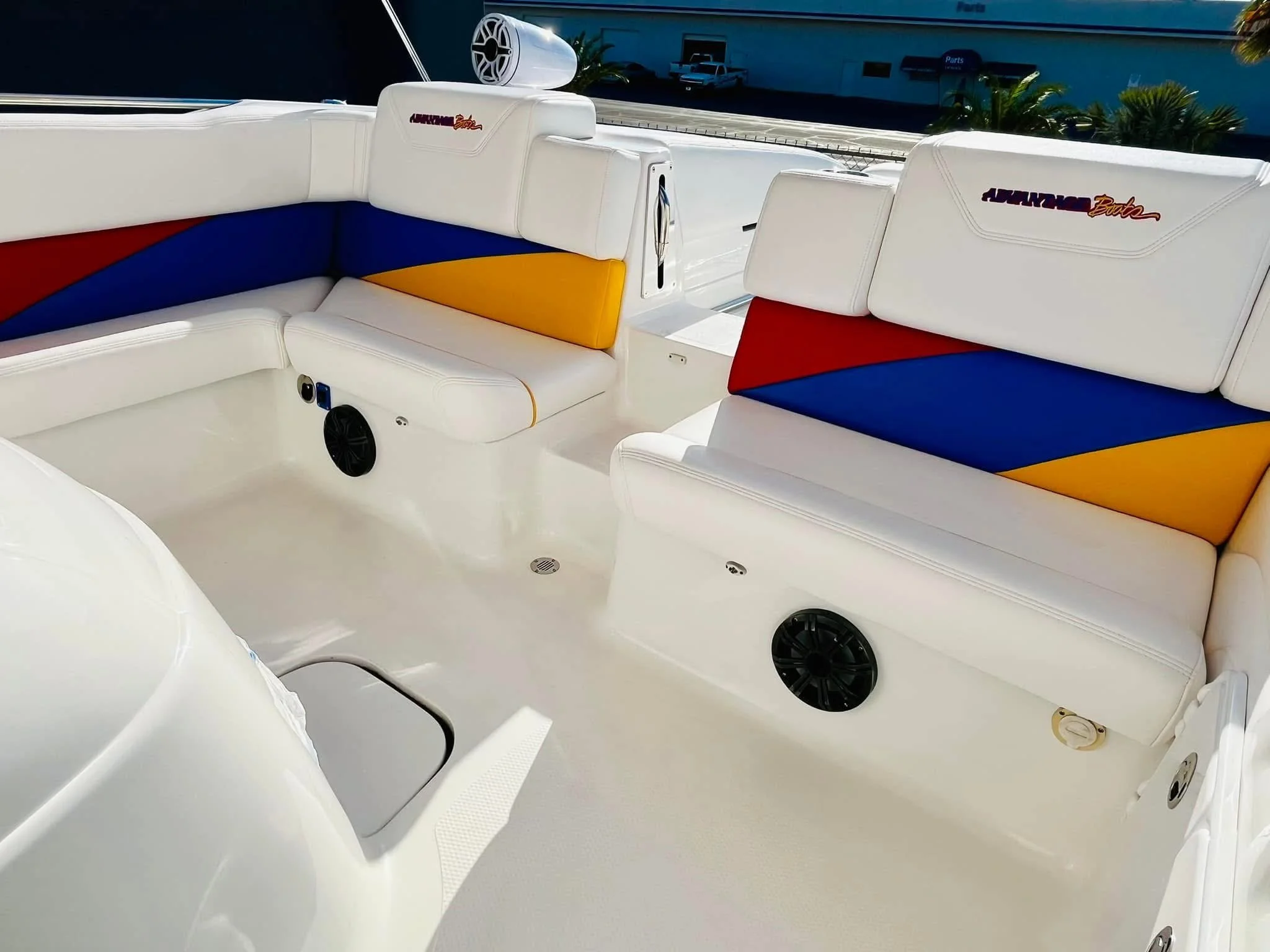 Interior of a white boat with colorful padded seating, including red, blue, and yellow sections, and built-in speakers.