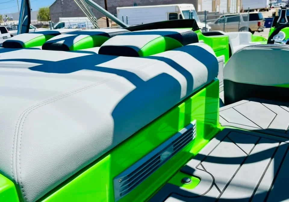 Close-up of boat seats with white and black cushions, accented with bright green, on a boat docked outdoors during the daytime.