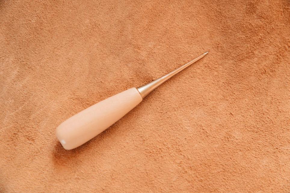 Awl tool for hide tanning with tapered steel point and wood handle on tanned hide background