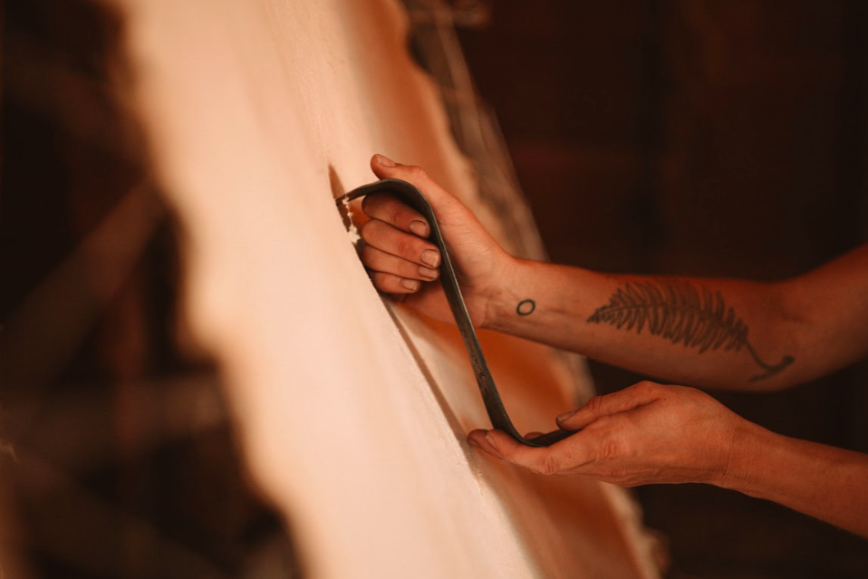 Two hands holding Hand-forged bevel-edged on each end S-scraper  made from forged steel in front of stretched hide