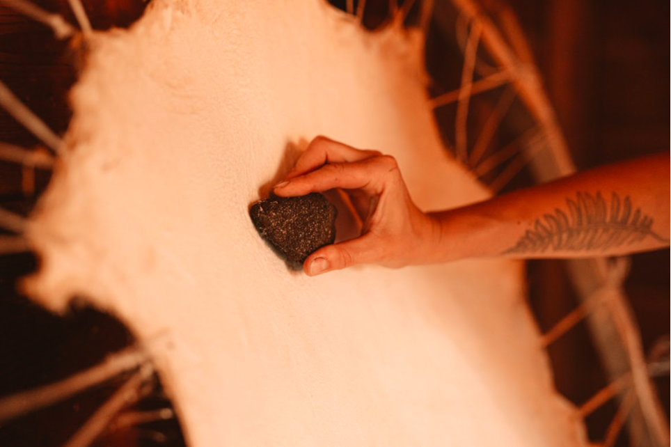 Hand holding volcanic pumice stone tool stretched hide on frame