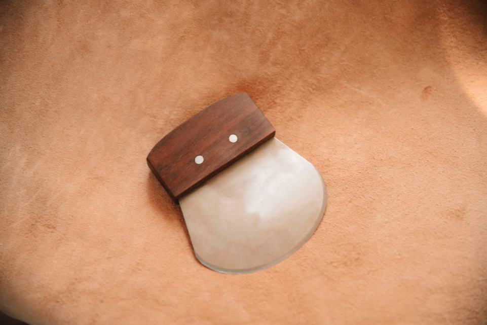 Single bevel head knife showing polished bevel and rich wood grain handle. on tanned hide backdrop