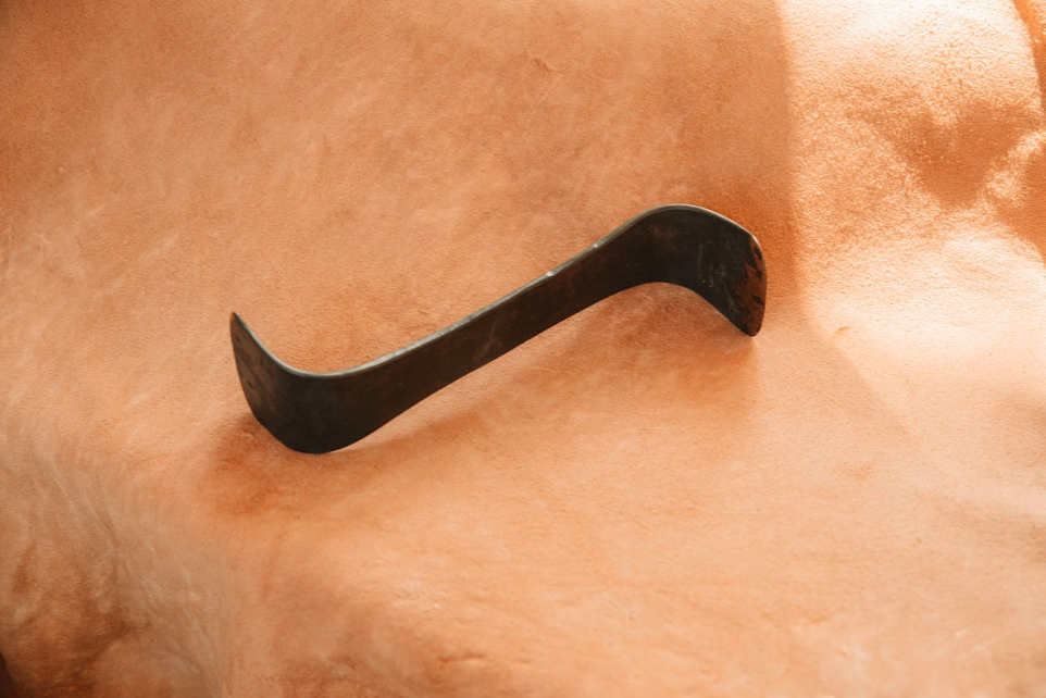 Hand-forged bevel-edged on each end S-scraper  made from forged steel on tanned hide background