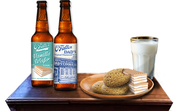Two bottles of Fallon brand vanilla wafer and DAD'S cookie root beer, a glass of milk, oatmeal cookies, and layered cake slices on a wooden tray.