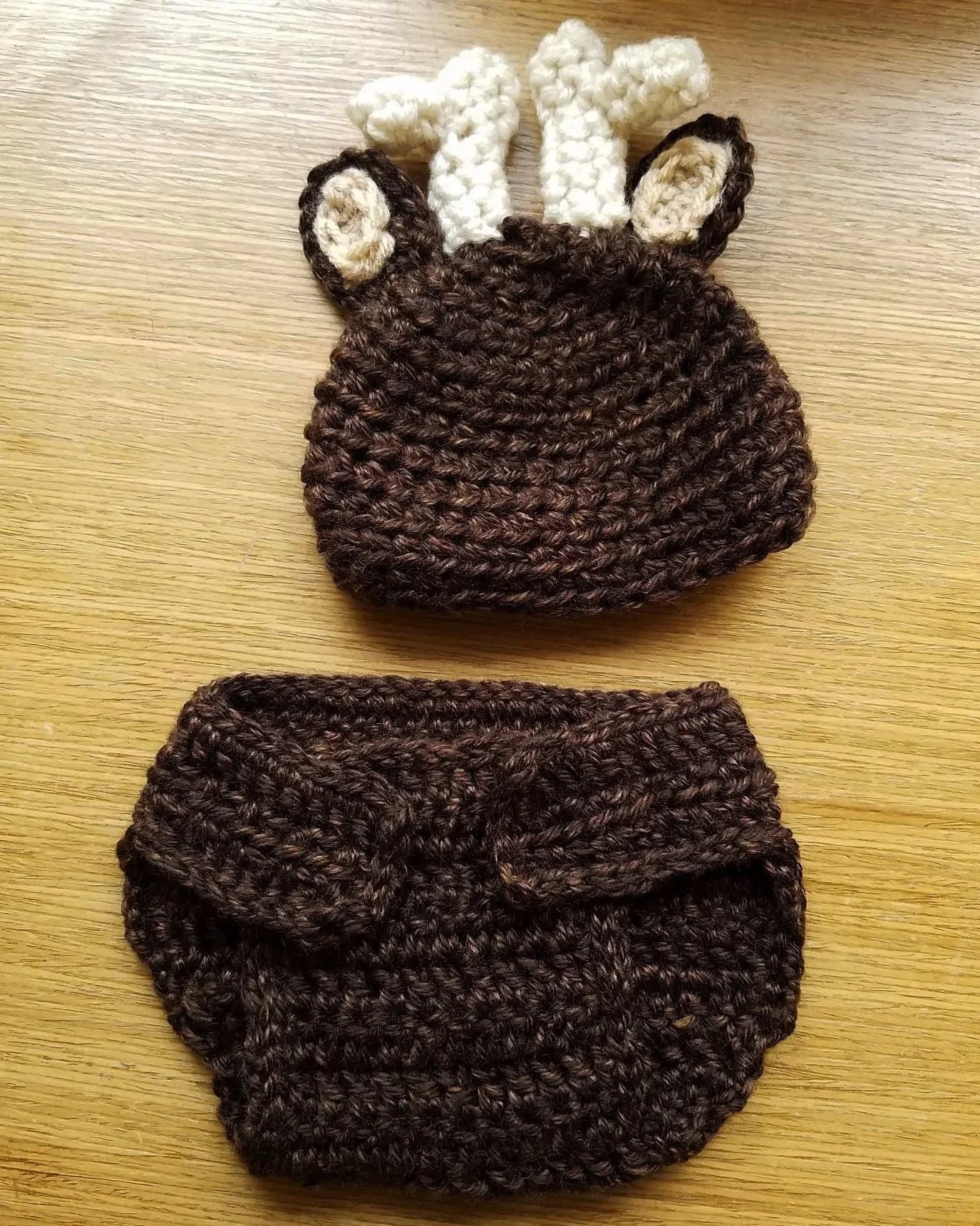Two crocheted winter accessories: a dark brown beanie hat with a ribbed brim and a matching headband, a brown and black striped knit hat, and a white and brown giraffe-shaped crochet Christmas ornament.