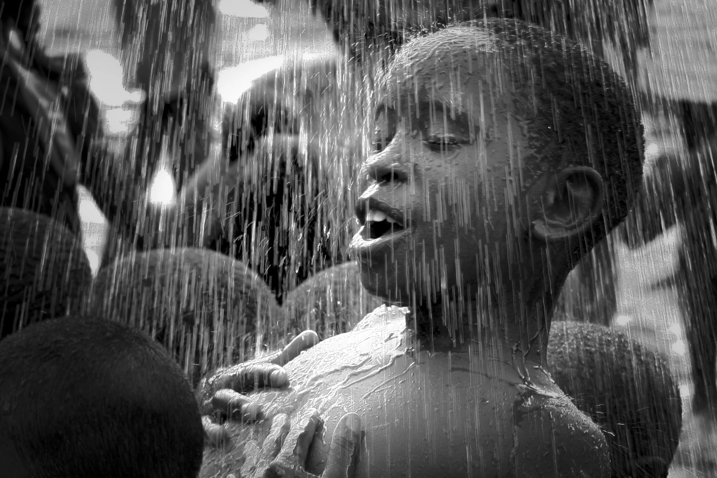 A young child with wet hair smiling and playing in a water fountain or waterfall. The image is in black and white.