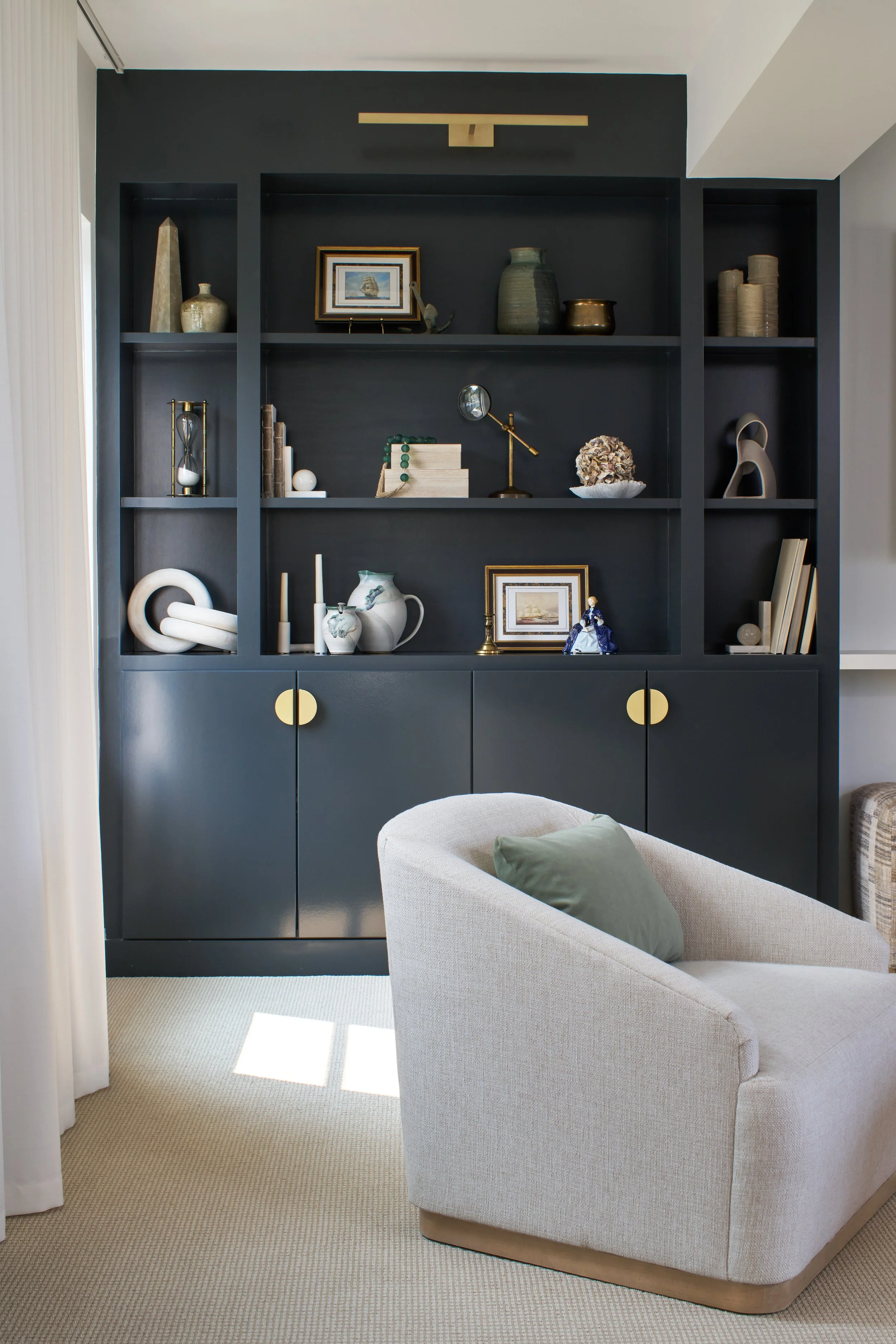 Custom moody built-in shelving, with décor, brass library light, geometric hardware, and accent chair with white oak base
