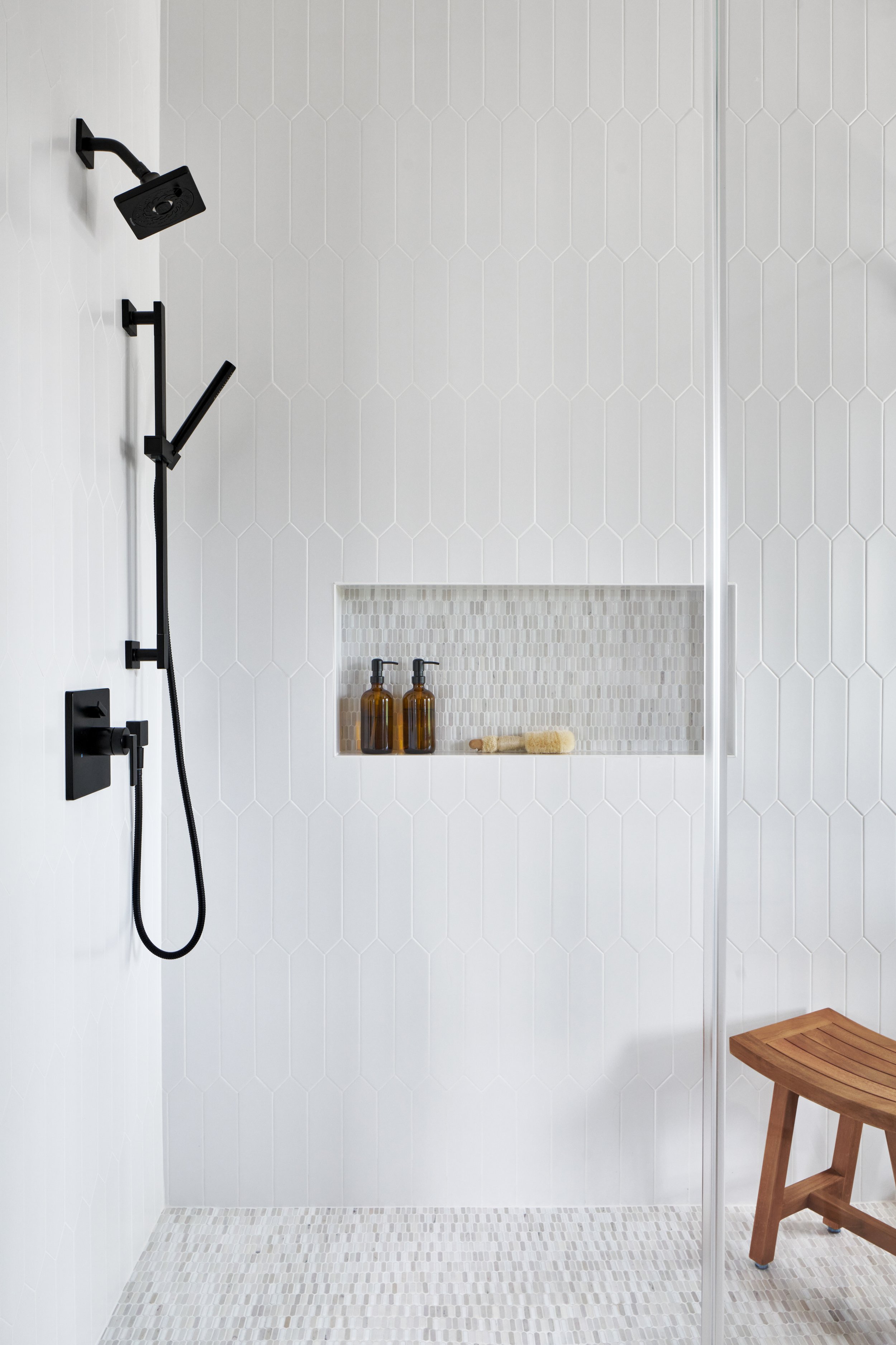 Modern bathroom with glass shower, matte black fixtures, and natural geometric tile palette