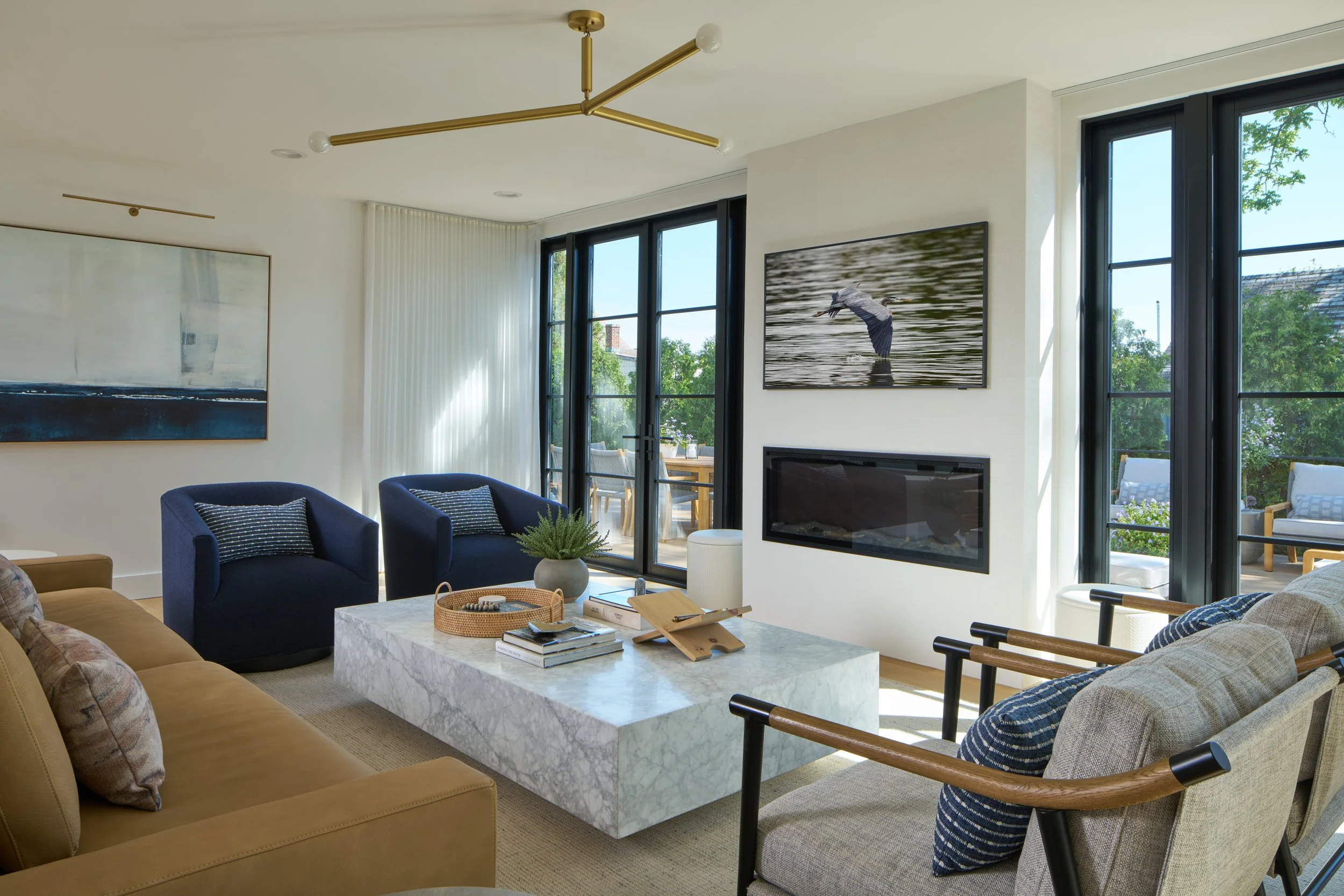 Bright transitional living room with plaster fireplace, sculptural lighting leather sofa, blue accents, and marble coffee table