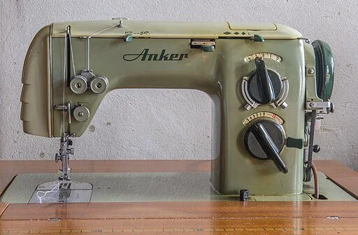 An antique green Anker sewing machine on a wooden table against a gray wall.