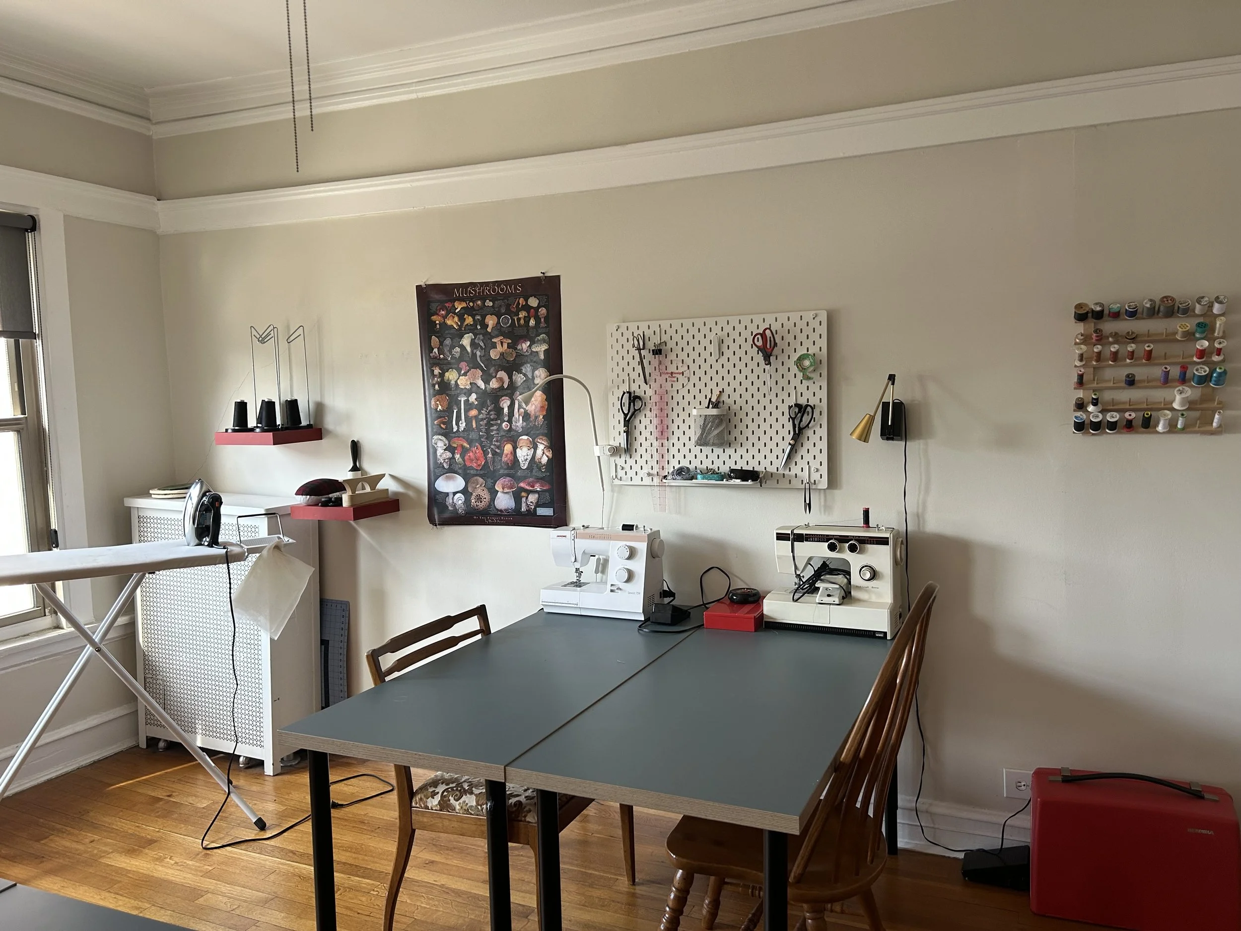A sewing and craft room with work tables, sewing machines, scissors, thread spools, and organizational posters on the wall.