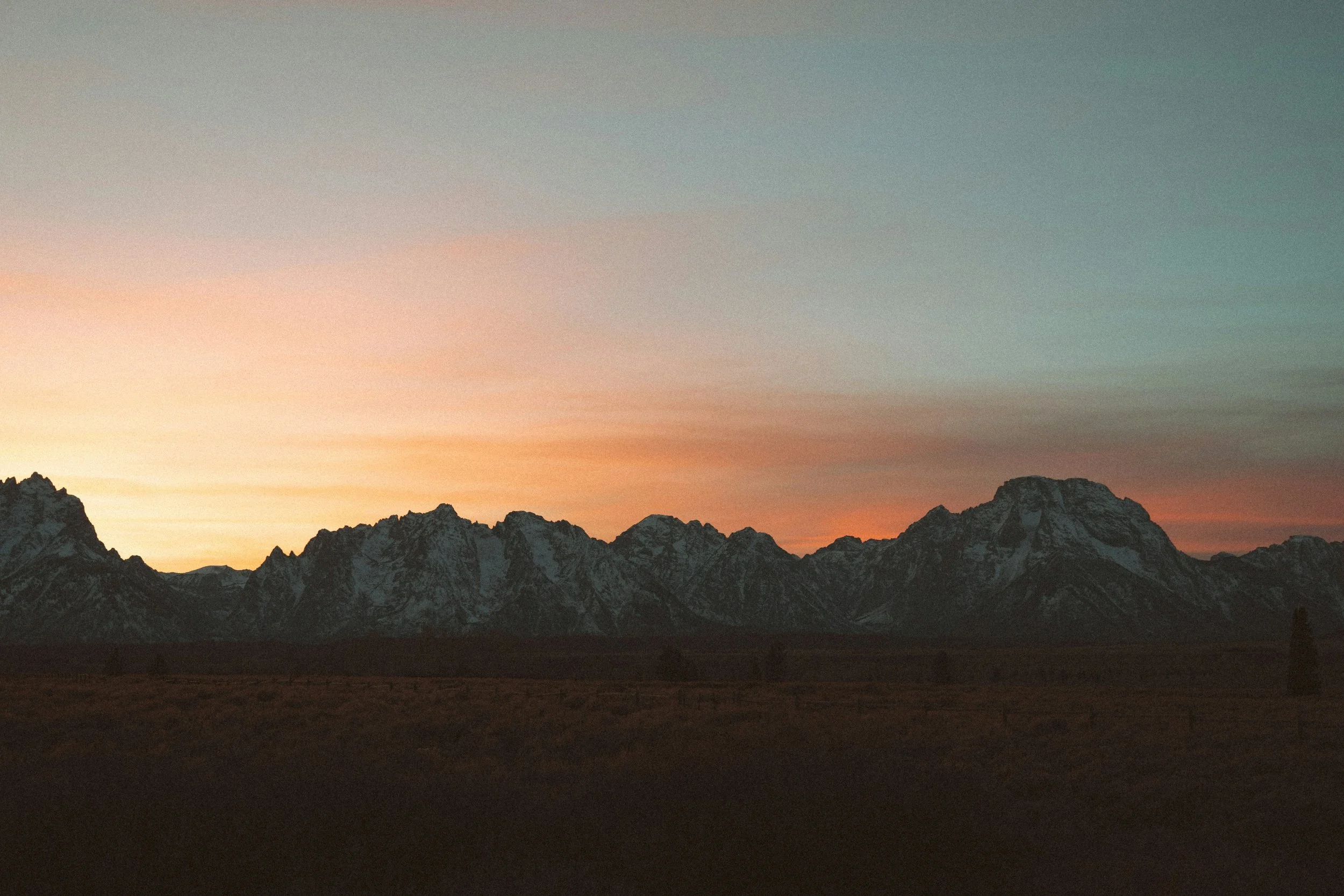 Sunset over snow-capped mountains with a clear sky and orange and pink hues in the background.