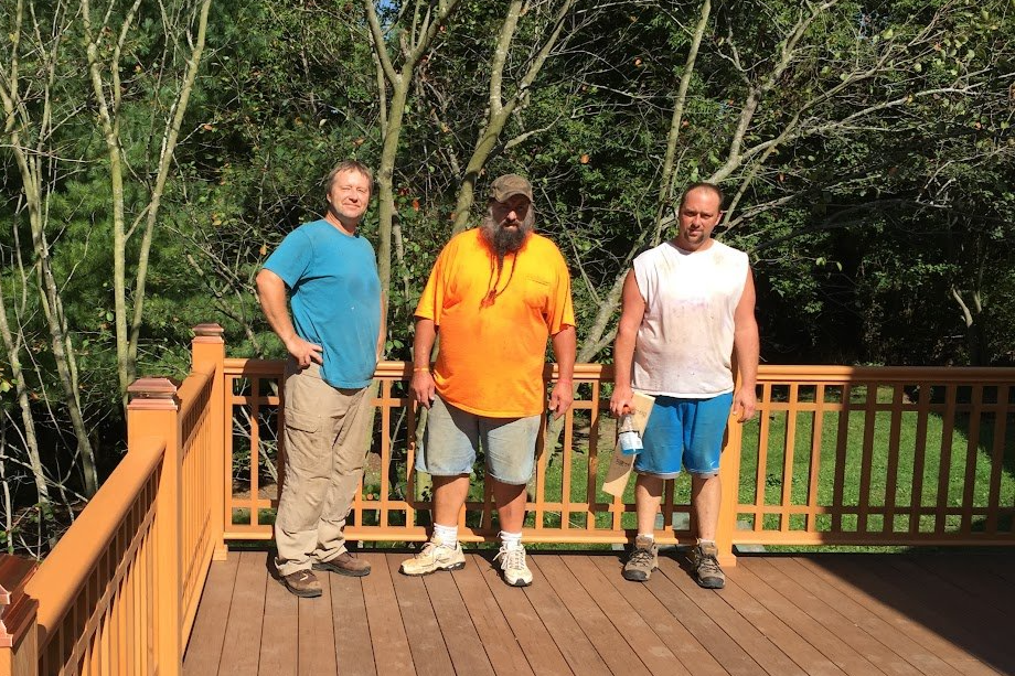 Three men standing on a wooden deck with trees in the background.
