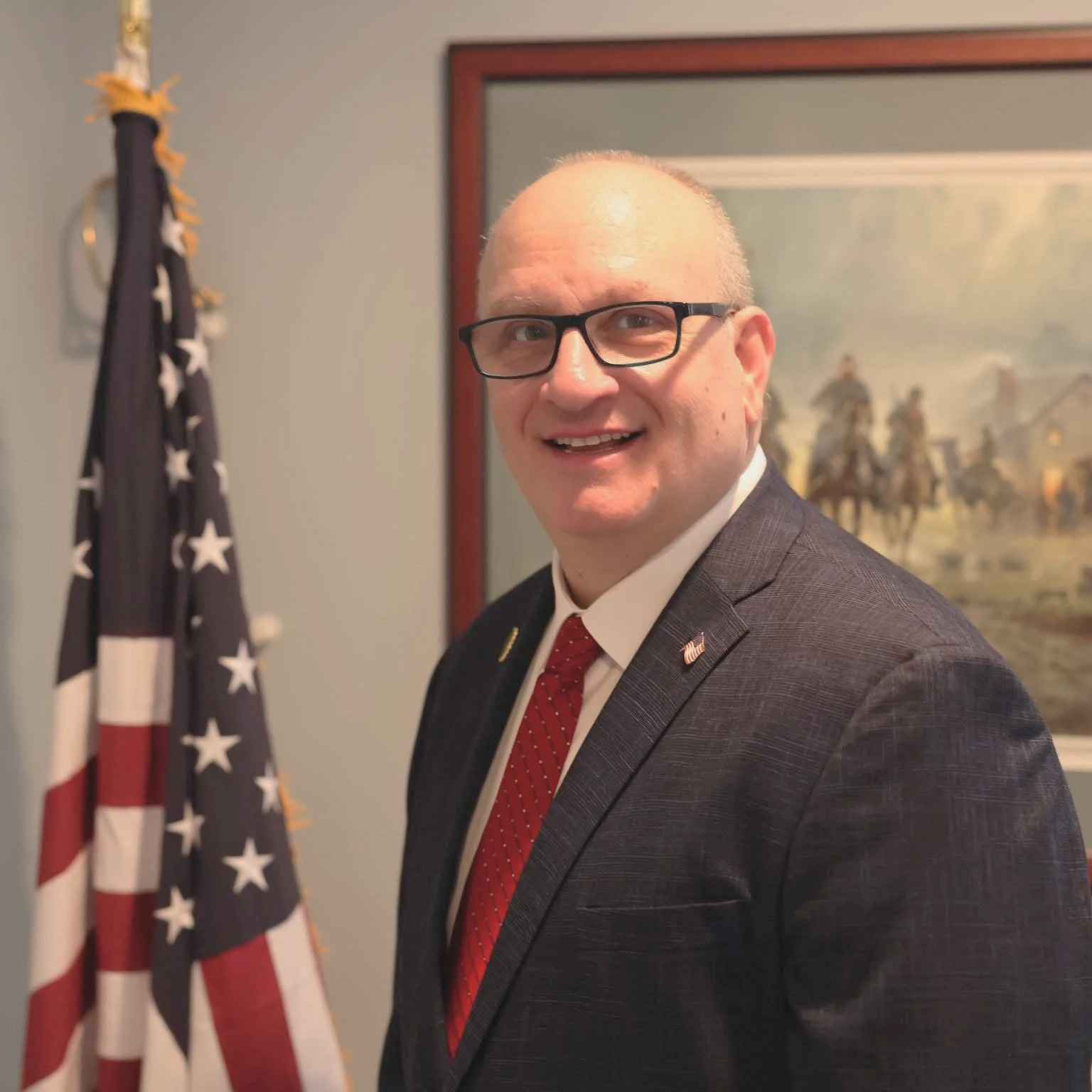 Man in glasses sitting at a panel with a nameplate that reads Robert Trotta, district representative, District No. 13.
