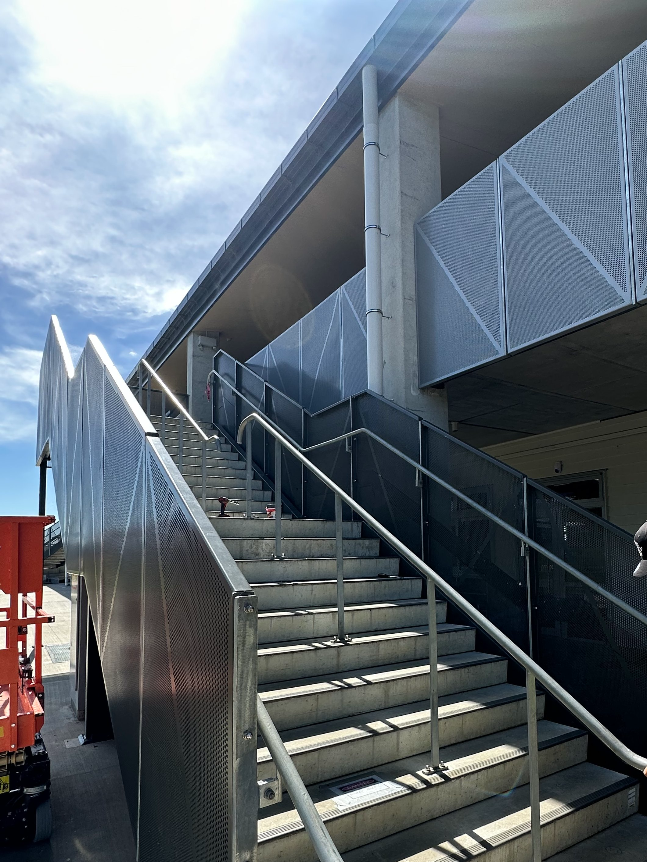 Outdoor concrete staircase with metal railings and mesh panels at a modern building under a partly cloudy sky.
