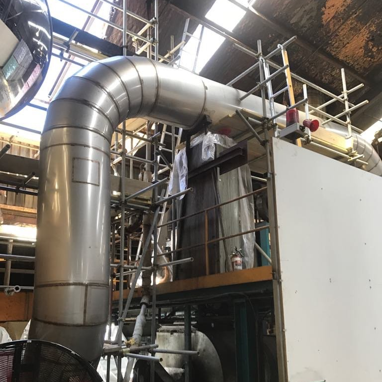Indoor industrial setting with large metal pipes, scaffolding, and machinery.