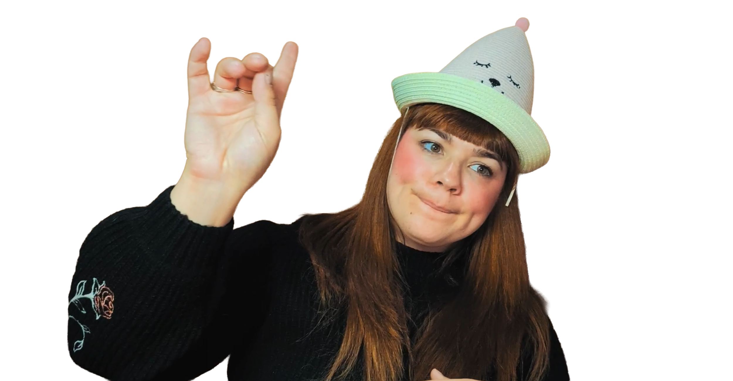A young woman with long brown hair, wearing a black sweater with an embroidered rose on the sleeve, making an OK gesture with her right hand. She has on a beige hat with a face embroidered on it, closed eyes, and a tiny nose, resembling a sleeping face.