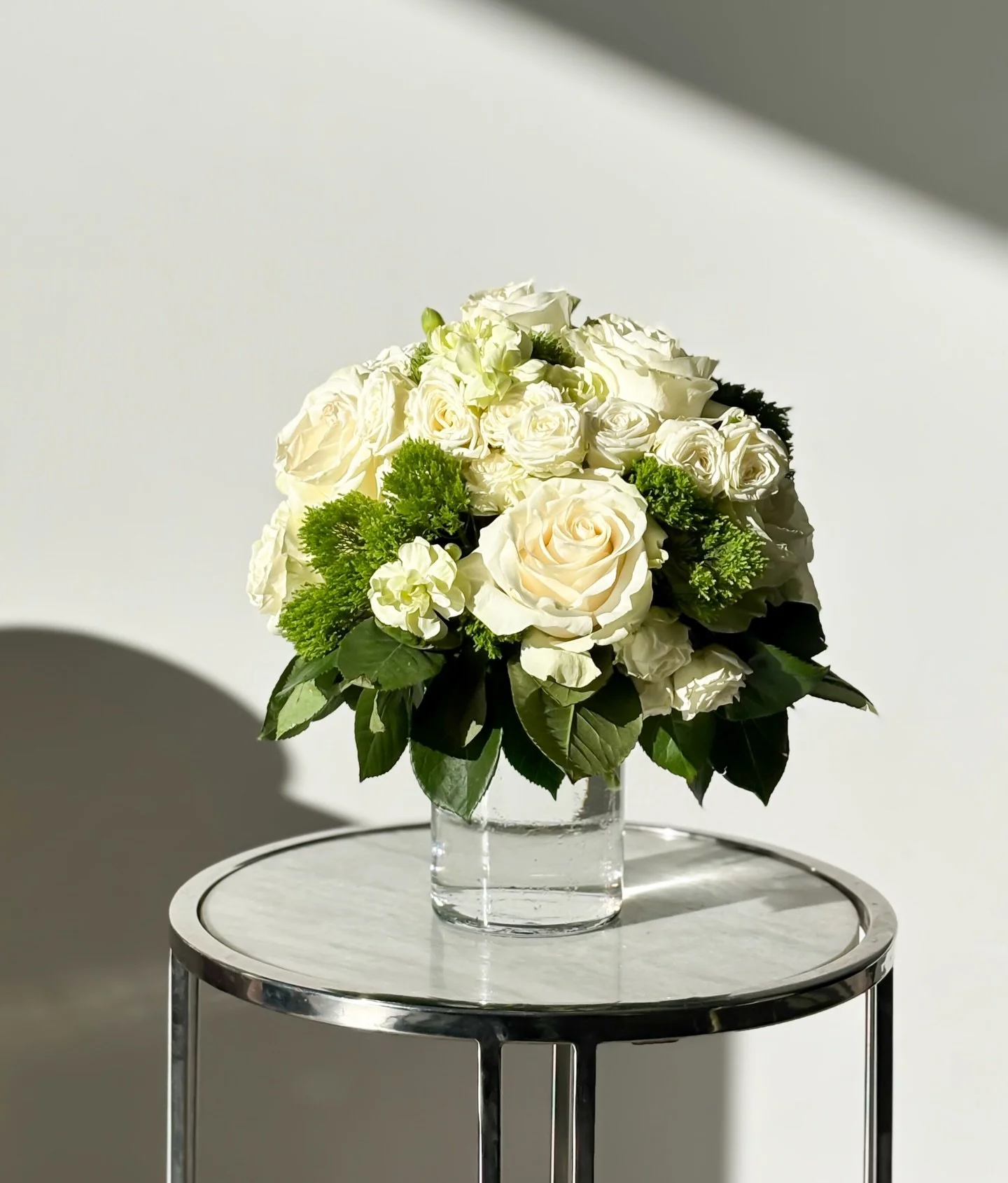 La luz de la ma&ntilde;ana revela la pureza de este arreglo en blanco: rosas aterciopeladas, toques verdes que aportan vida y un equilibrio que habla de calma y sofisticaci&oacute;n.

Un dise&ntilde;o pensado para espacios que buscan sentir la bellez