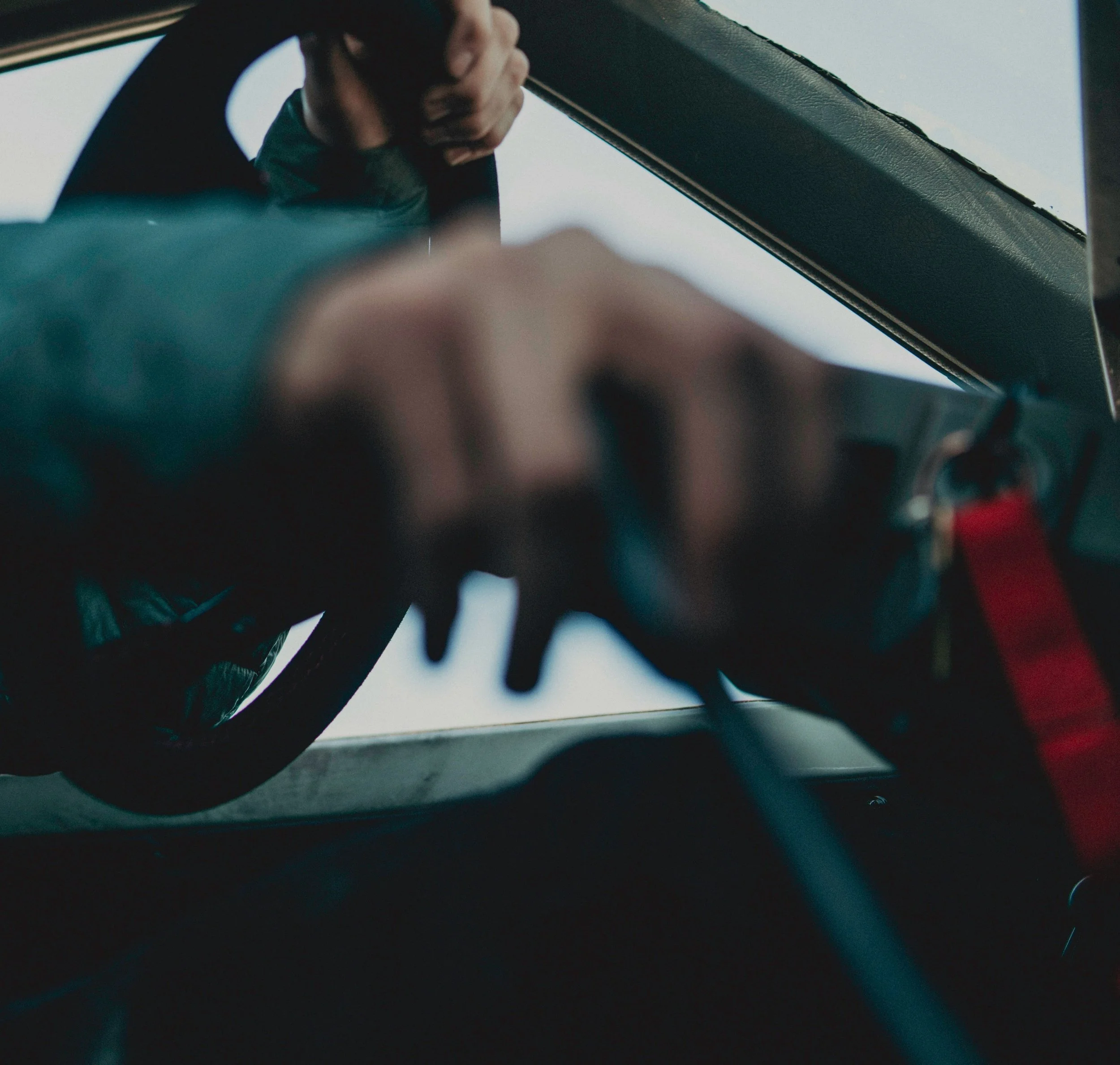 Close-up of a person's hand turning a key in a car ignition, with the steering wheel visible and the sky in the background.