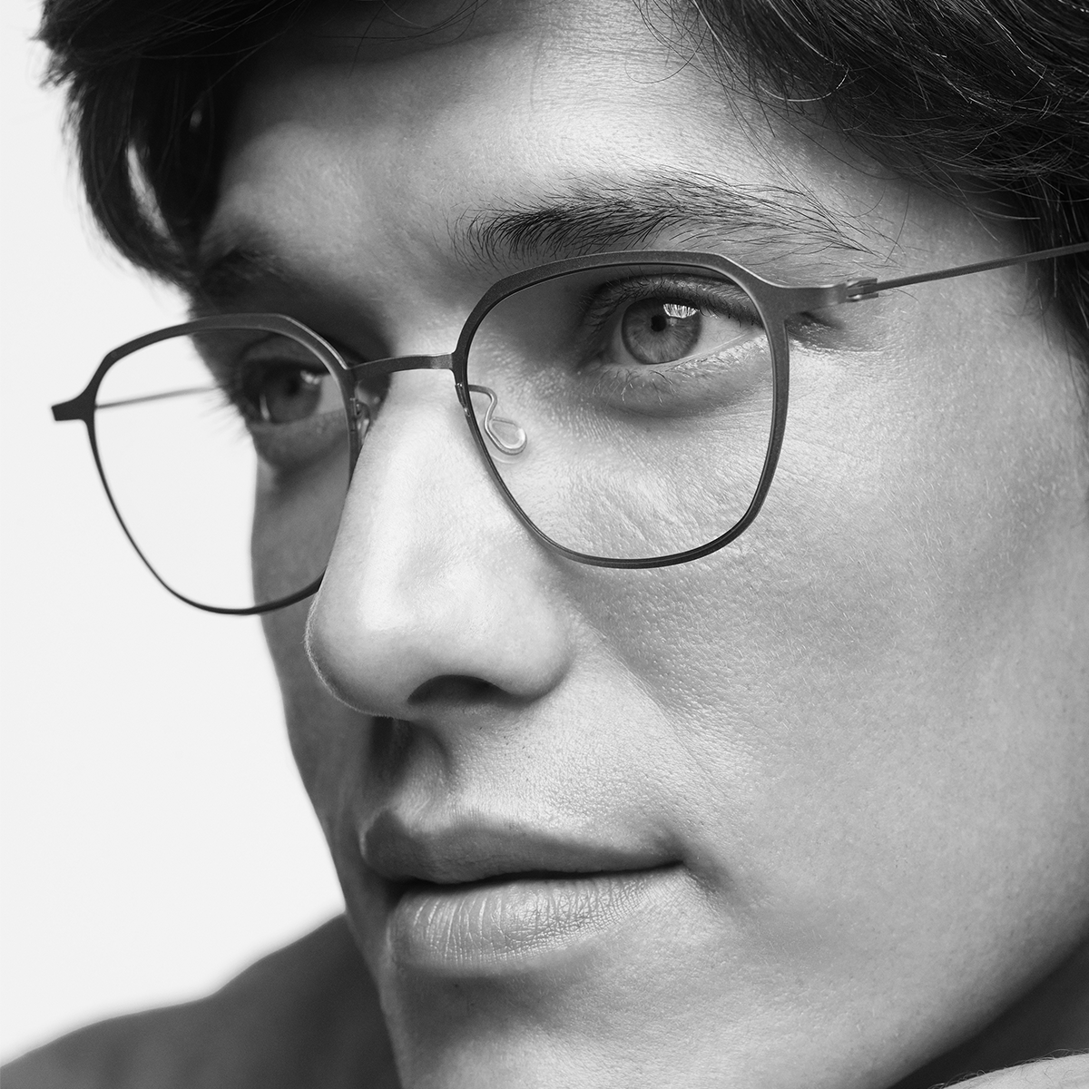 A close-up black-and-white photograph of a person wearing glasses, focusing on the face from the nose up, showing the eye, eyebrow, and part of the cheek.