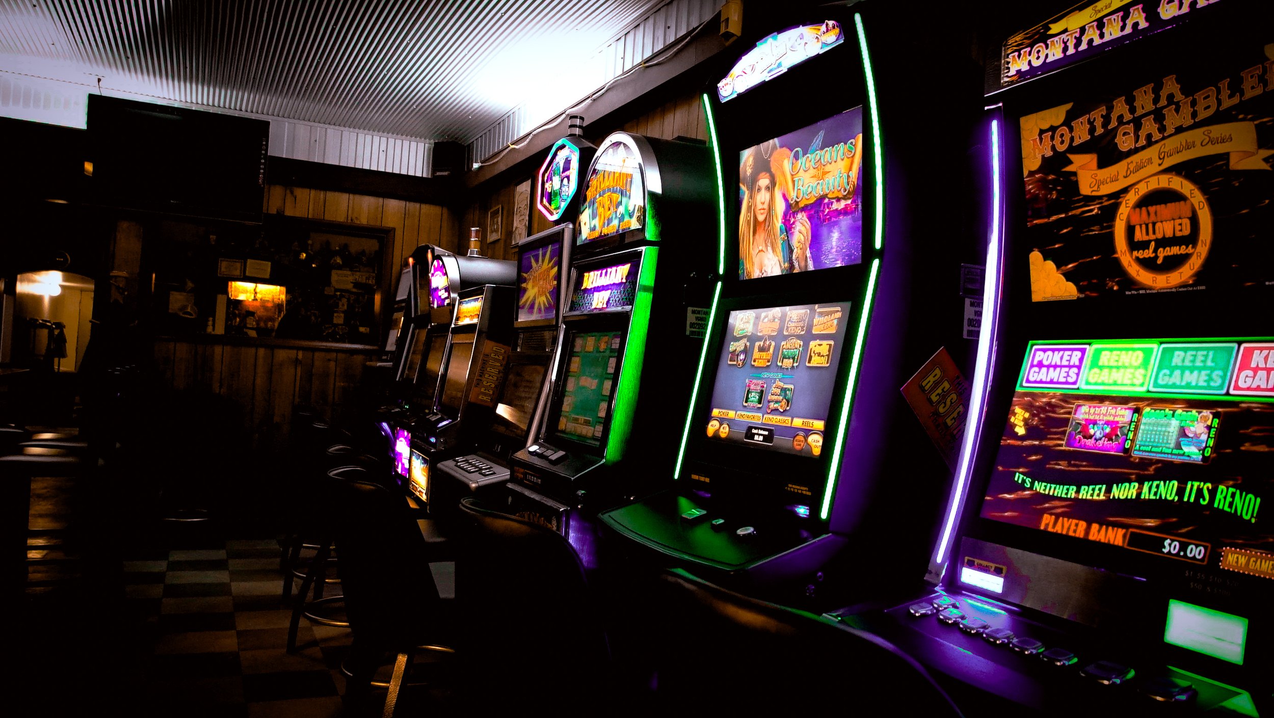 A row of brightly lit slot machines with colorful displays inside a dimly lit casino or gaming parlor.