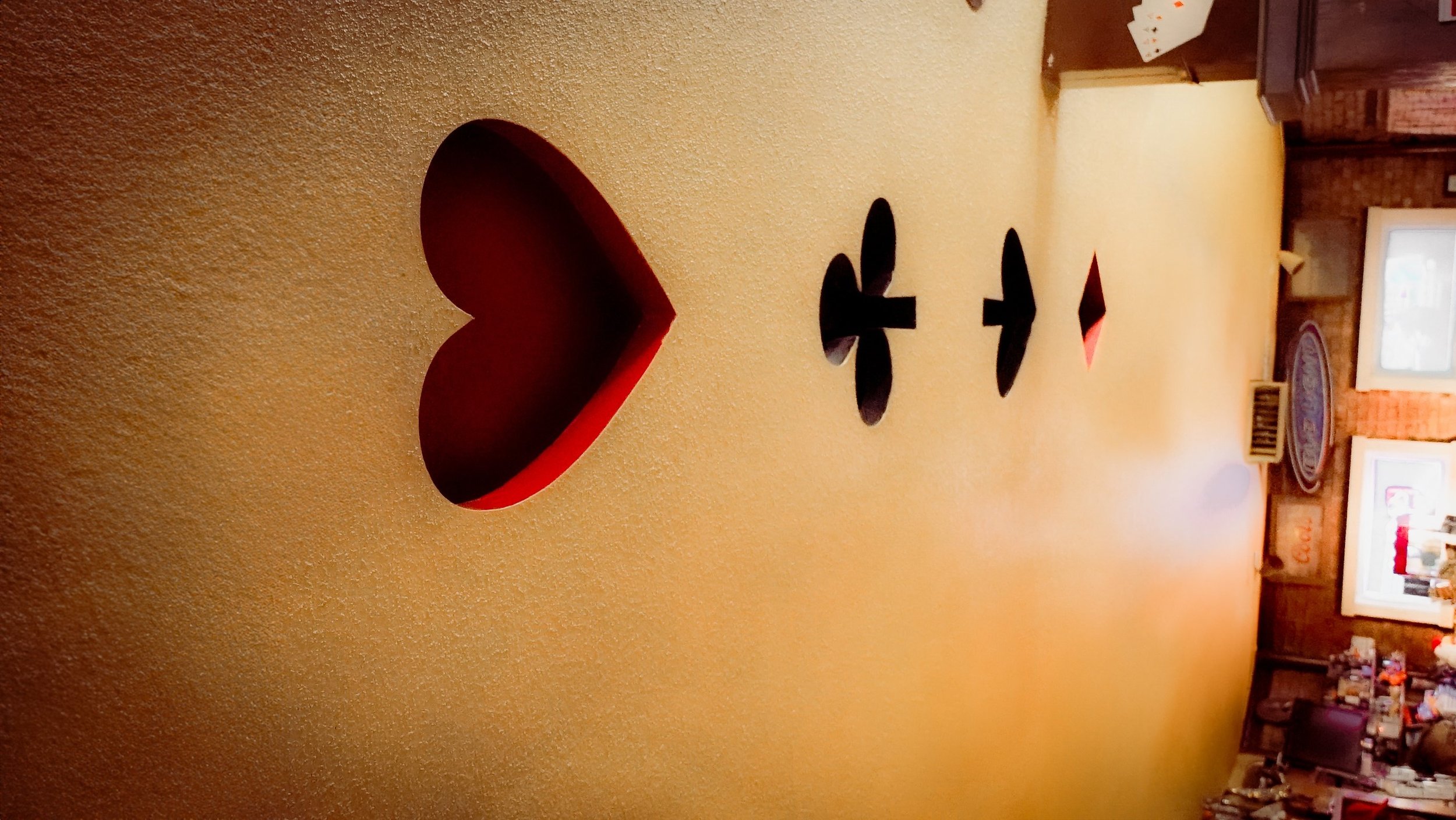 Decorative wooden heart and arrow shapes on a yellow wall in a restaurant, with a wooden sign in the background.