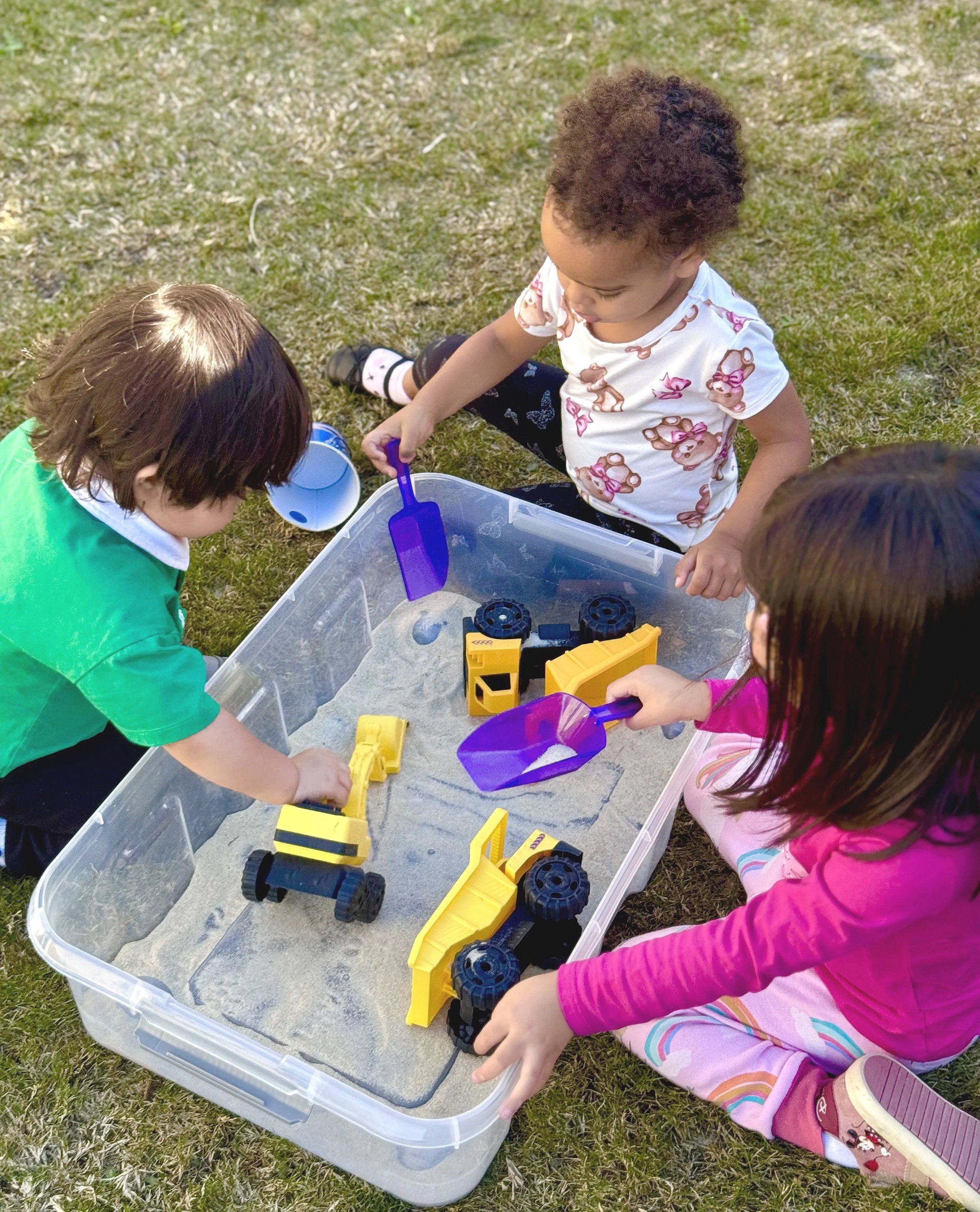 Three small kids playing outside with play sand and sand toys.