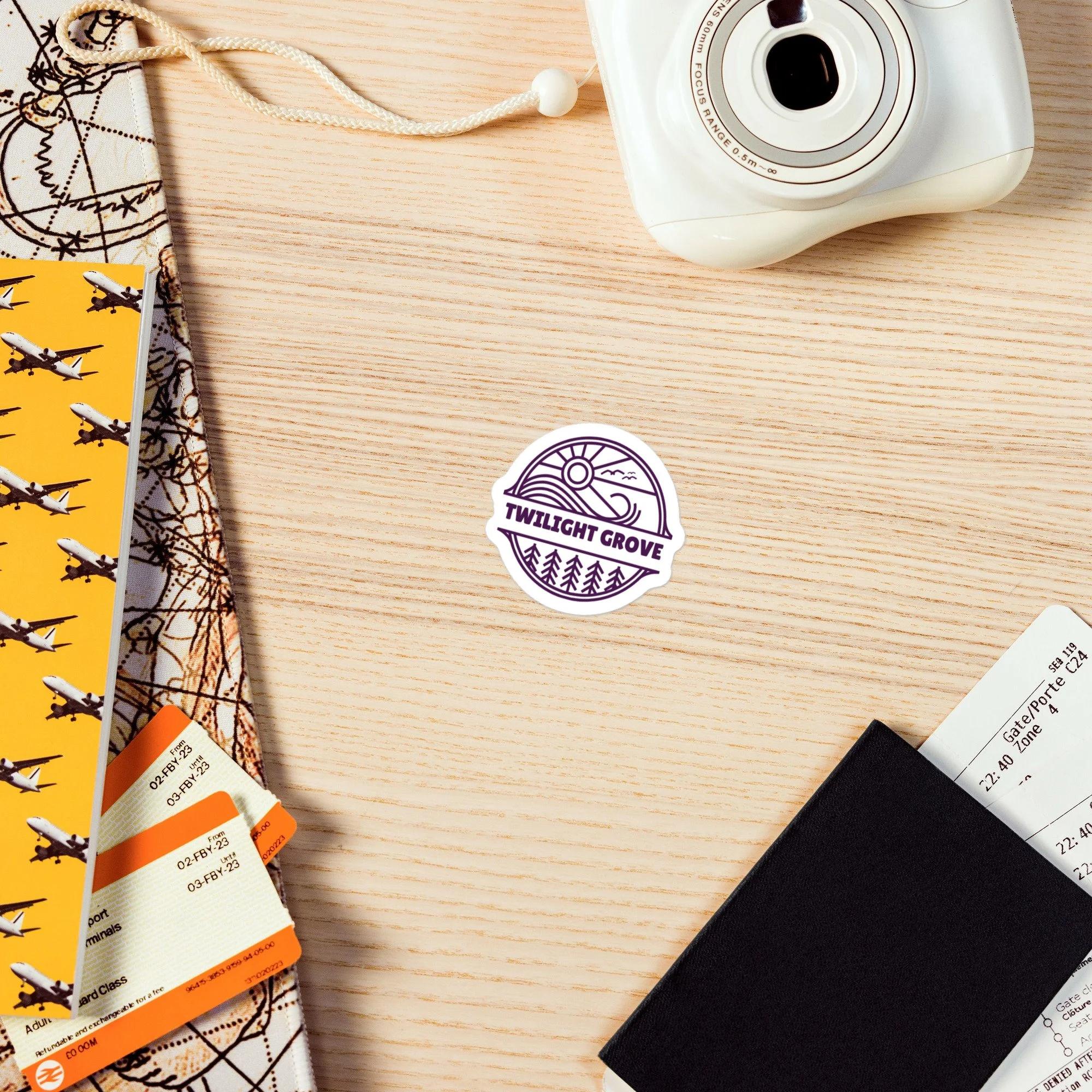 Twilight Grove Logo Sticker shown on a travel-themed desk flatlay with camera and passport