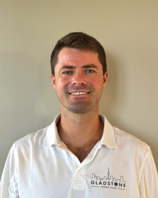 A young man with short brown hair and light skin, smiling, wearing a white polo shirt with a 'Gladstone Tennis Club' logo, standing in front of a plain light-colored wall.