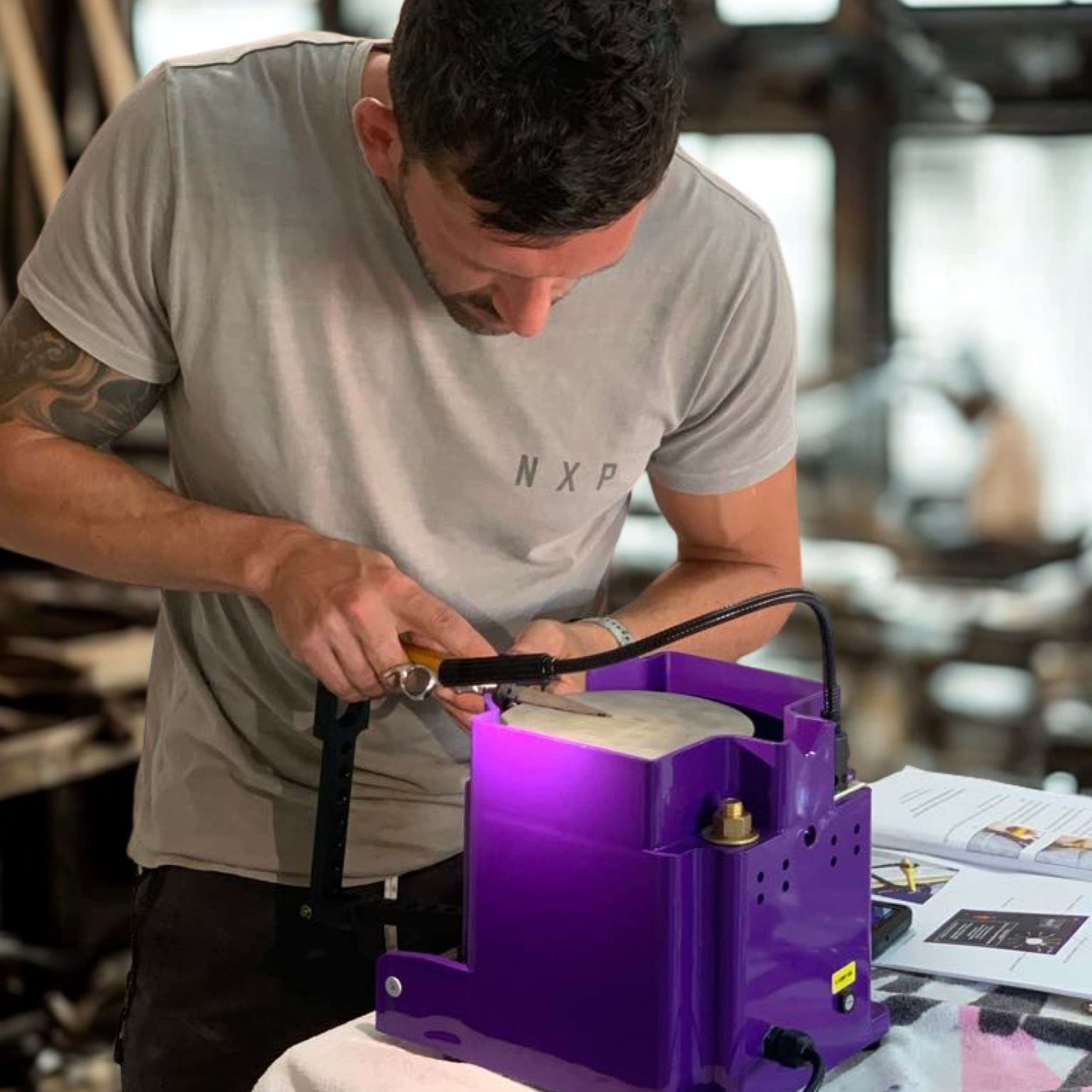 A man working in a workshop, using a UV light to inspect a piece of material placed inside a purple device.