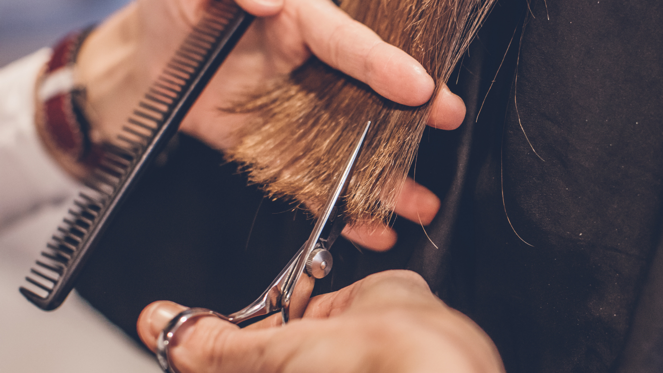 A hairdresser trims a person's hair with scissors and a comb.