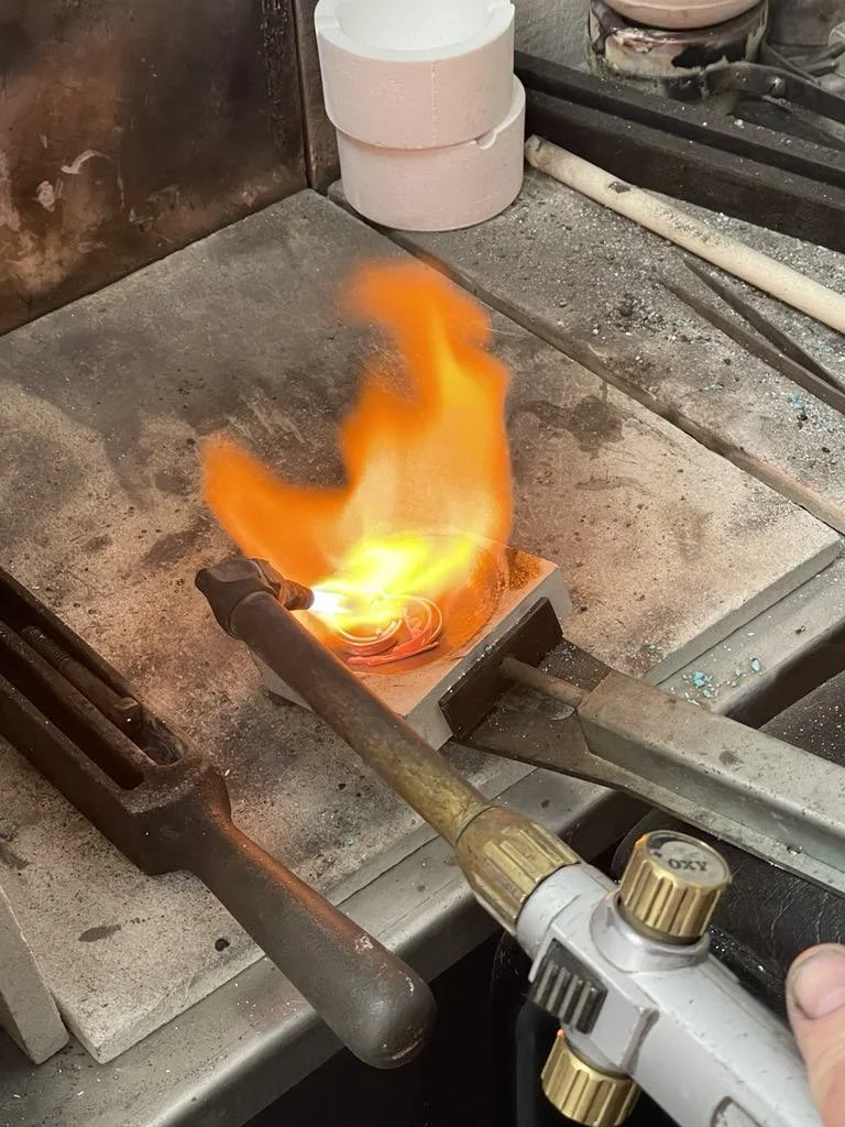 Torch heating a metal object with flames and bright yellow glow in a workshop setting.