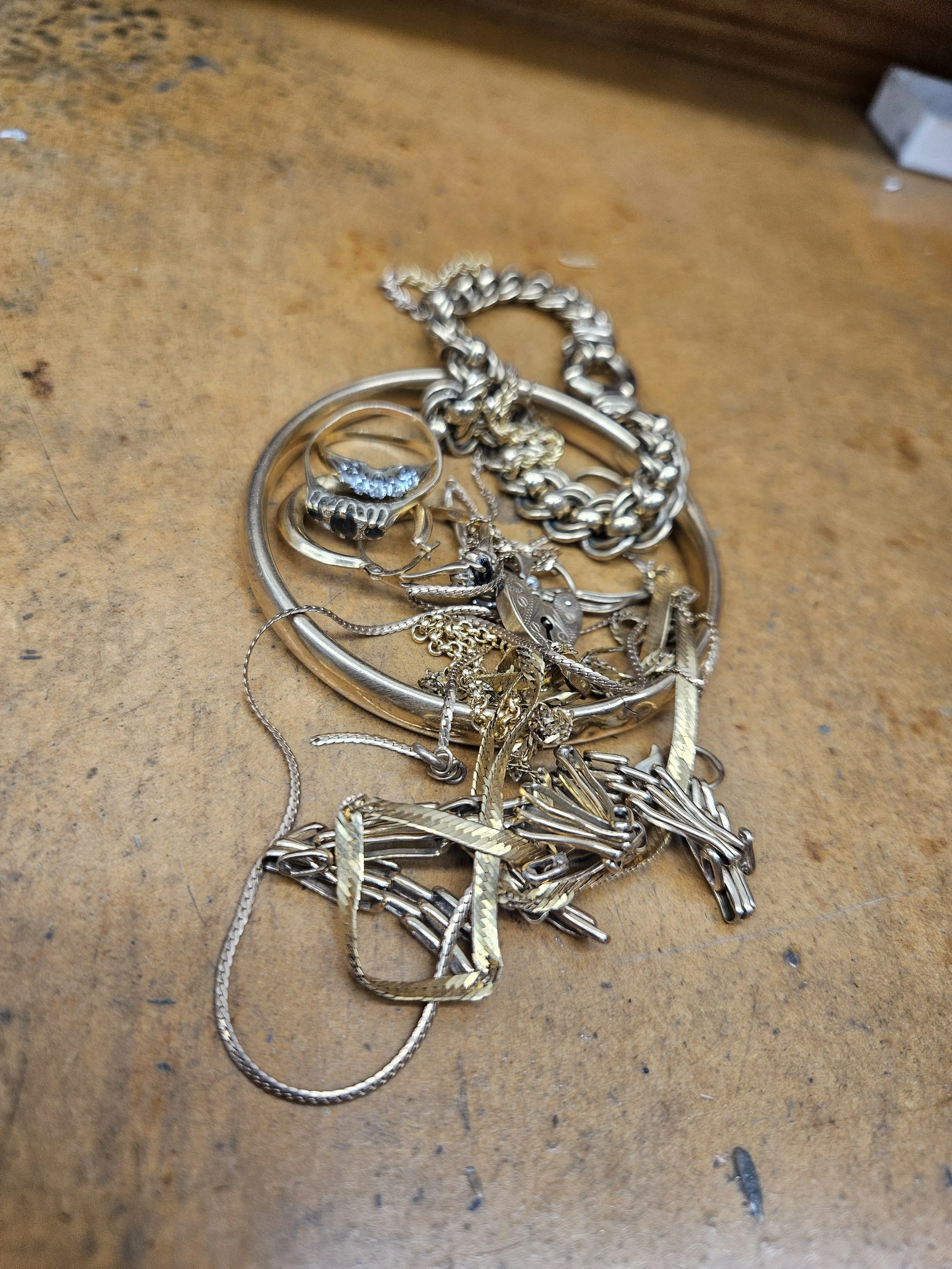 A pile of assorted silver jewelry, including rings, chains, and bracelets, on a worn wooden surface.