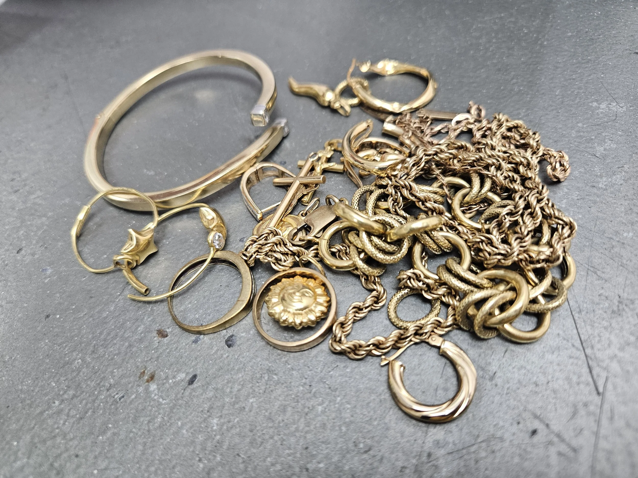 A collection of gold jewelry, including chains, rings, bracelets, and earrings, scattered on a gray surface.