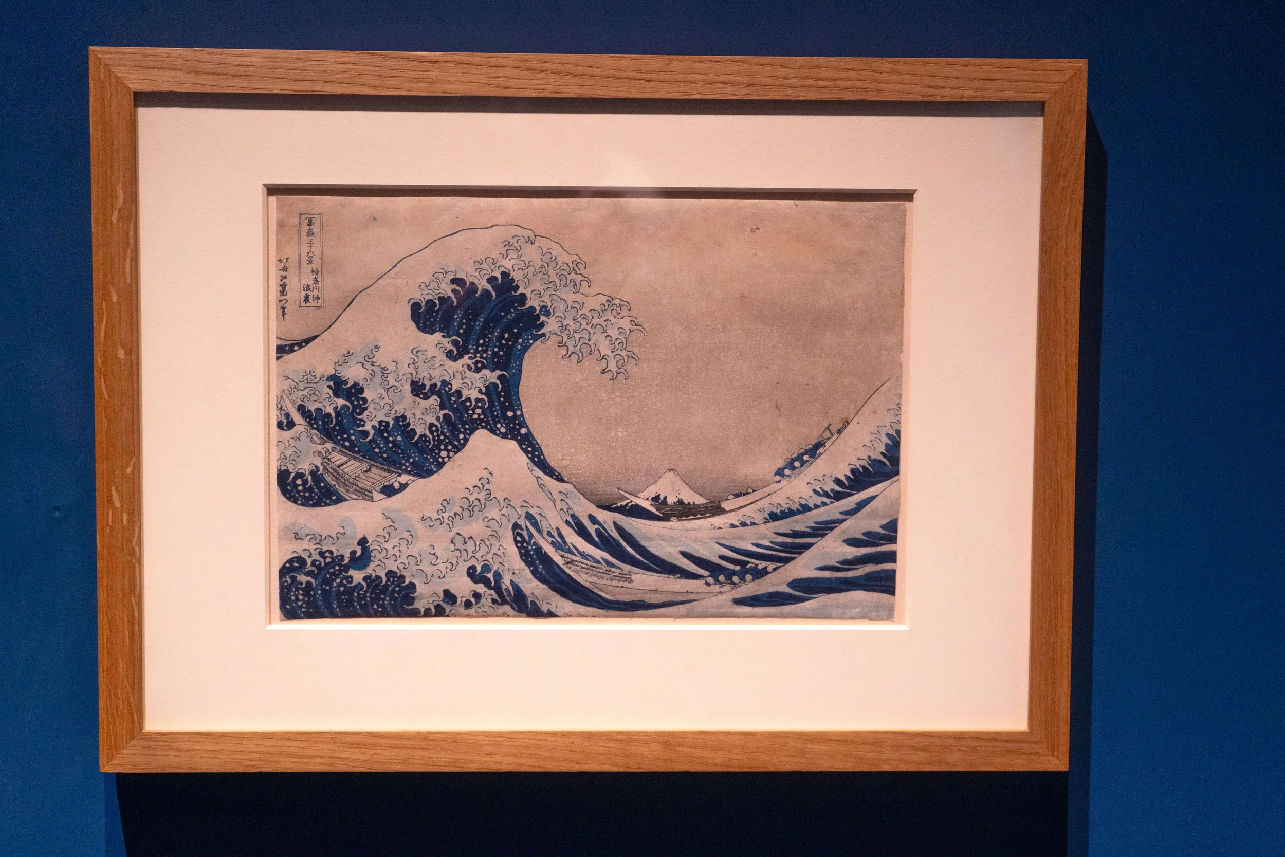 Una pintura de estilo ukiyo-e que representa una gran ola en el mar, con varias embarcaciones y la montaña Fuji al fondo.